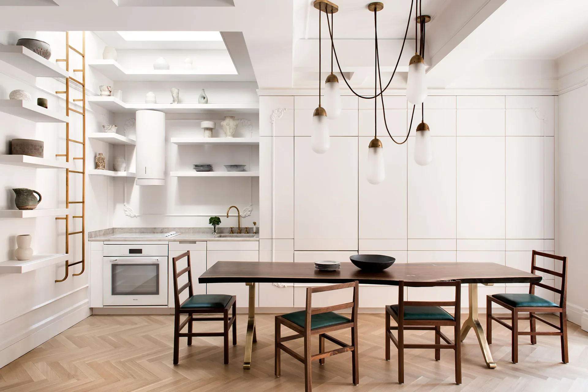 Minimalist dining space with white cabinetry, wood dining table, woven chairs, pendant lighting, and herringbone flooring by Cindy Coscoros.