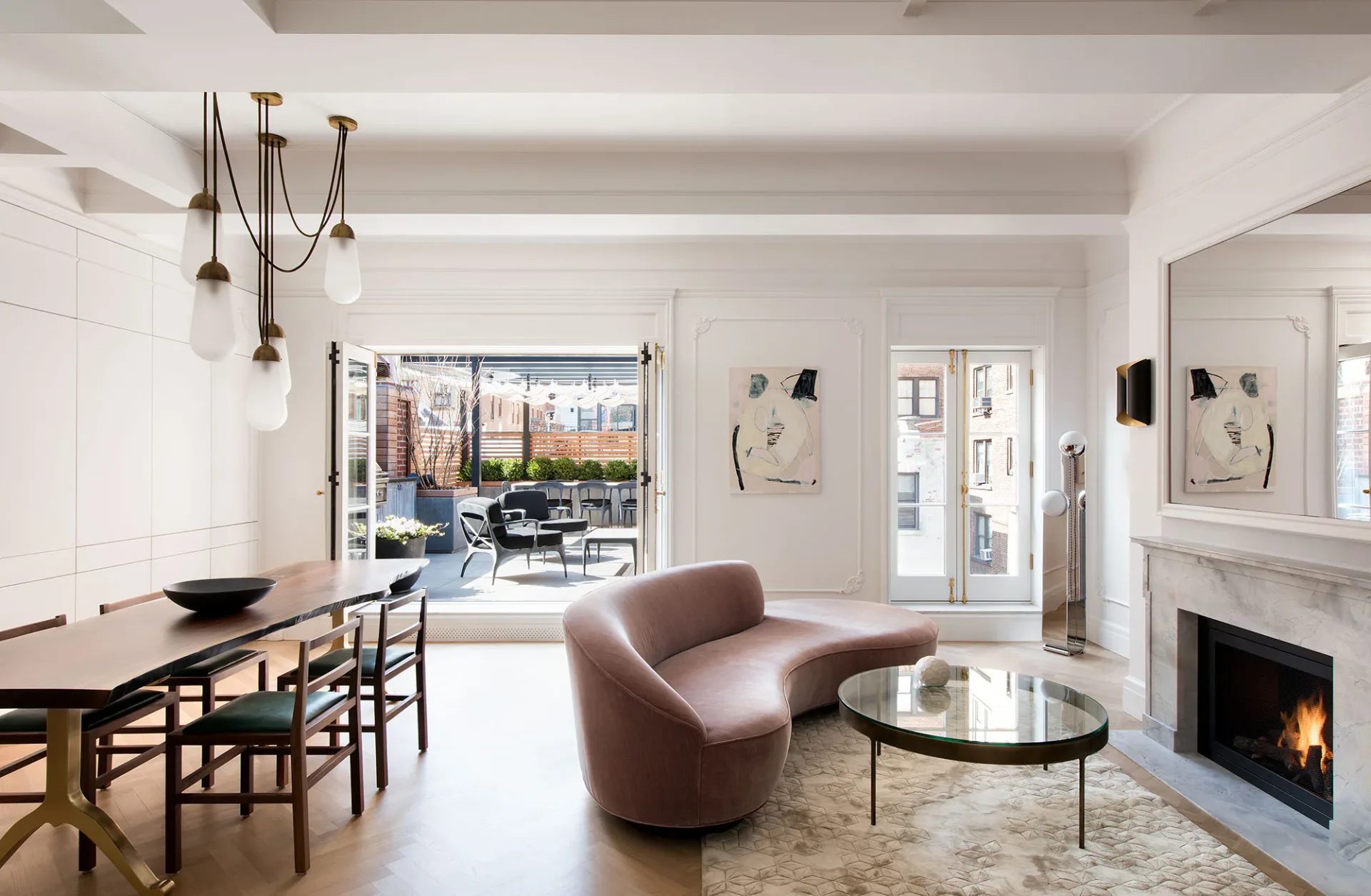 Modern living room with curved mauve armchair, round black coffee table, dining area with wooden chairs, fireplace, and large windows overlooking cityscape by Cindy Coscoros.