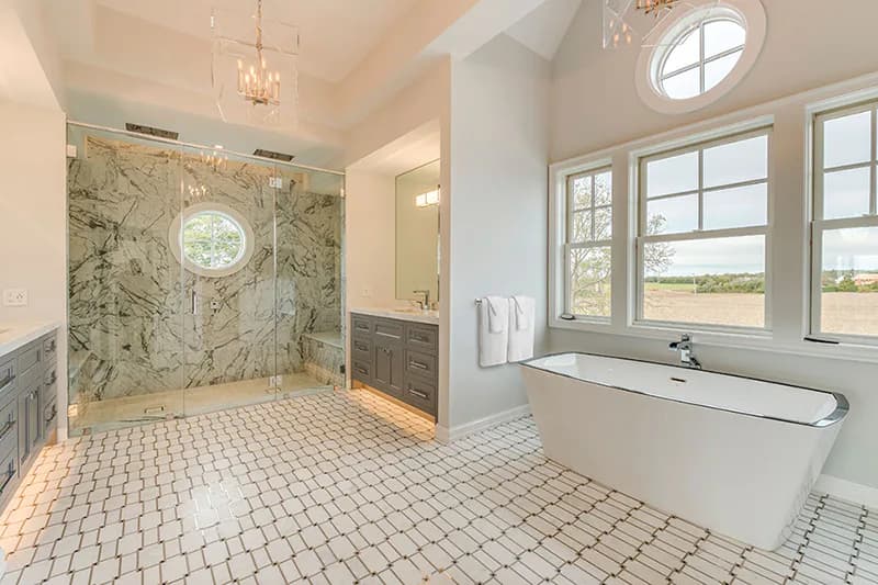 Luxurious master bathroom featuring marble shower enclosure, freestanding soaker tub, geometric tile flooring, and abundant natural light by Cindy Montgomery.