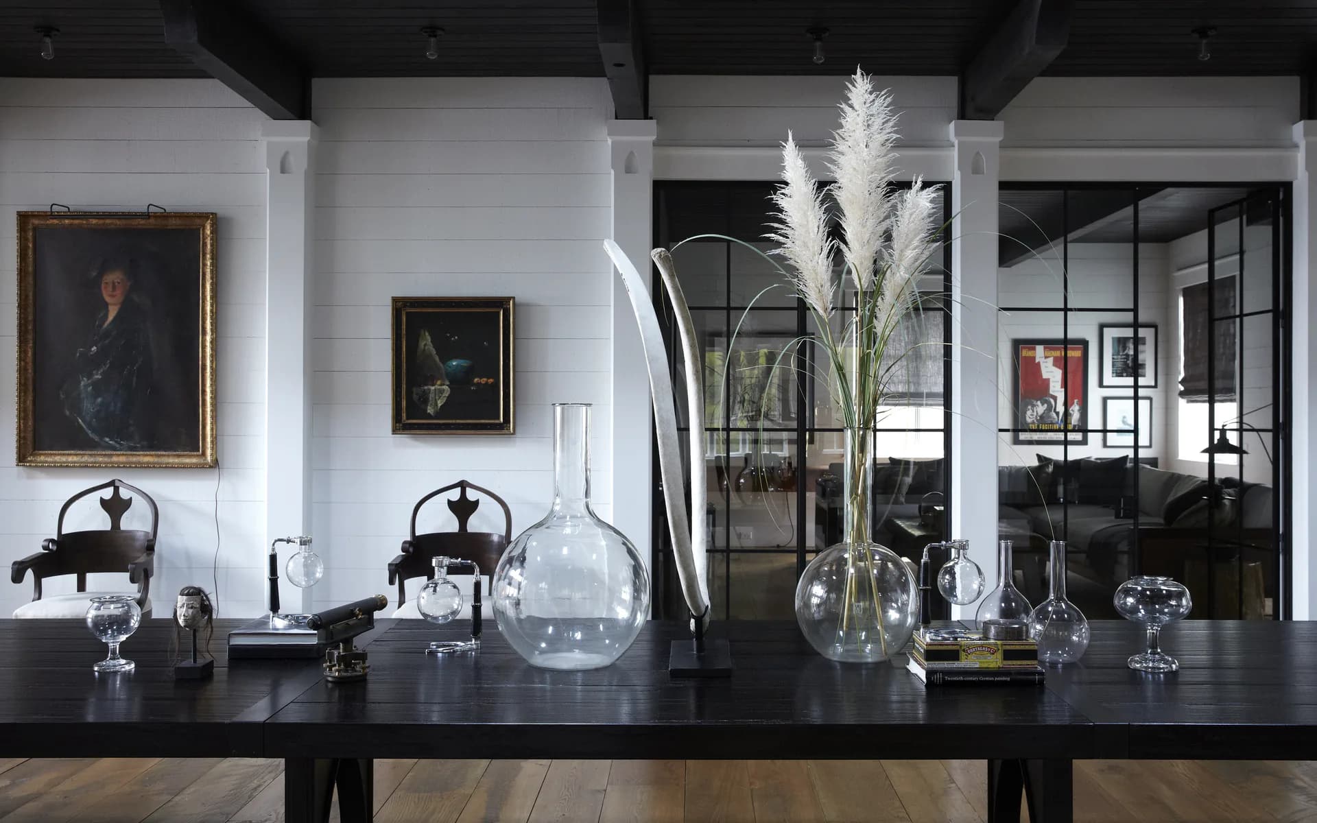 Modern interior with black counter displaying glass vessels and pampas grass, white brick walls, framed artwork, and glass partition visible in background by Claire Chung.