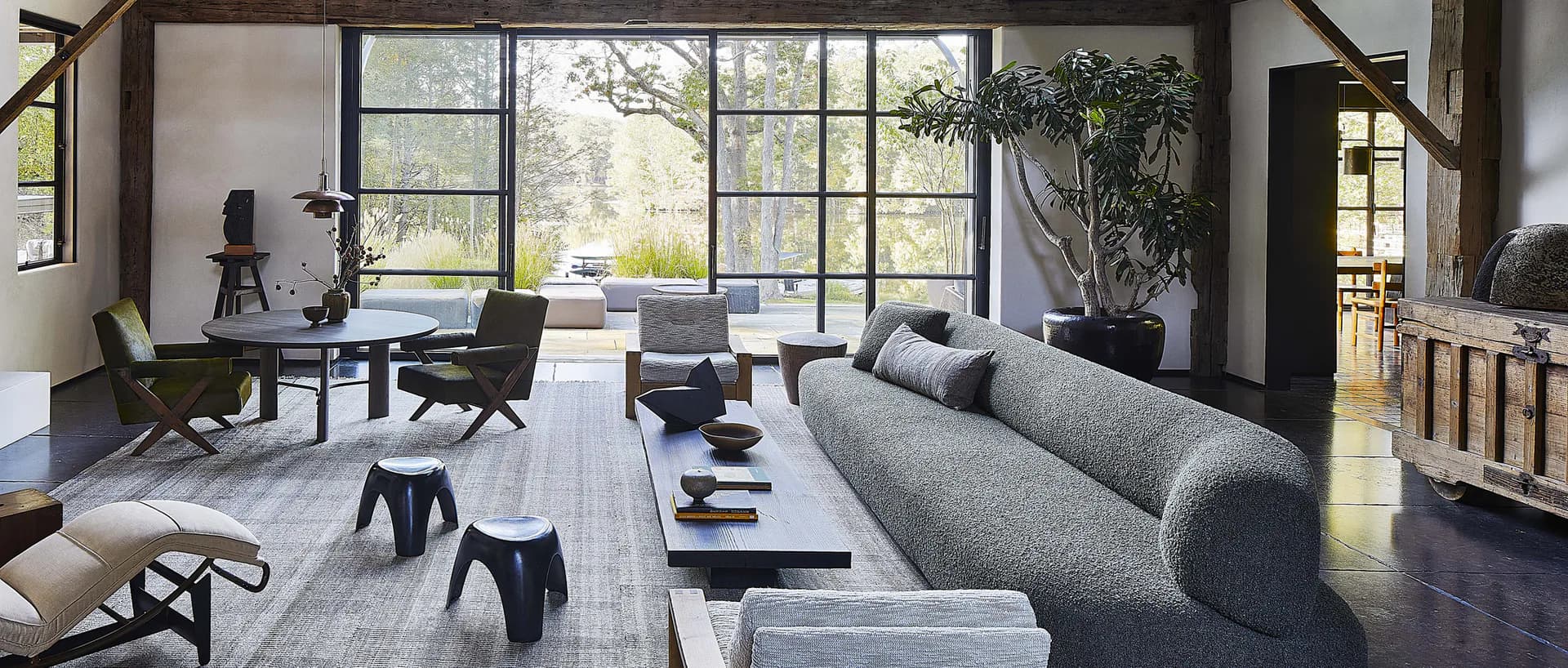Modern living room with gray sectional sofa, black sculptural furniture, and expansive gridded windows overlooking landscape by Claire Chung.