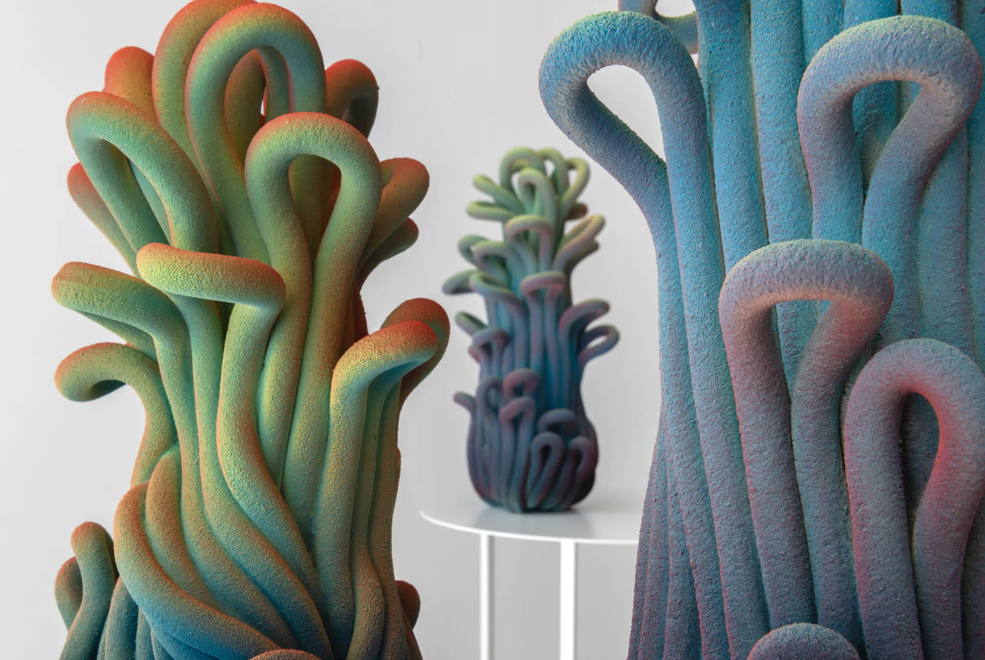 Three sculptural pipe forms with gradient blue-green-orange coloring and fuzzy texture rendered in 3D, by Claire Lindner.