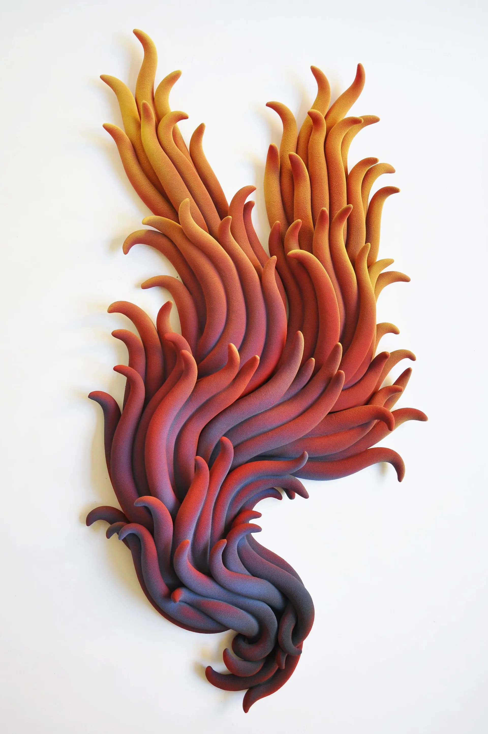 Layered sculptural wall installation with organic, flame-like forms in gradient colors from deep purple to orange and yellow, by Claire Lindner.