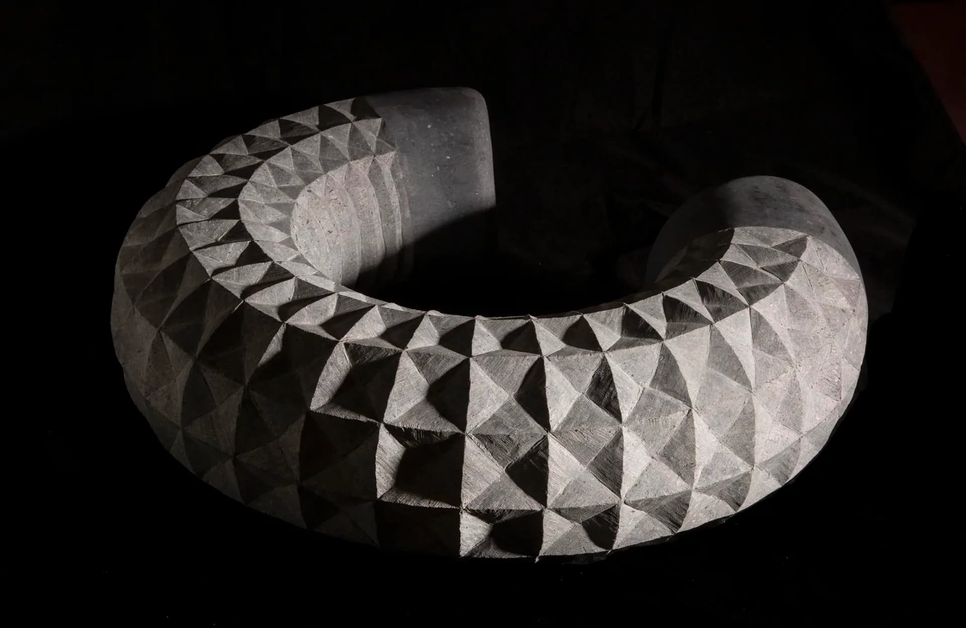 Curved sculptural form with geometric triangular surface patterns in grayscale, creating dimensional relief, by Claire McGovern.