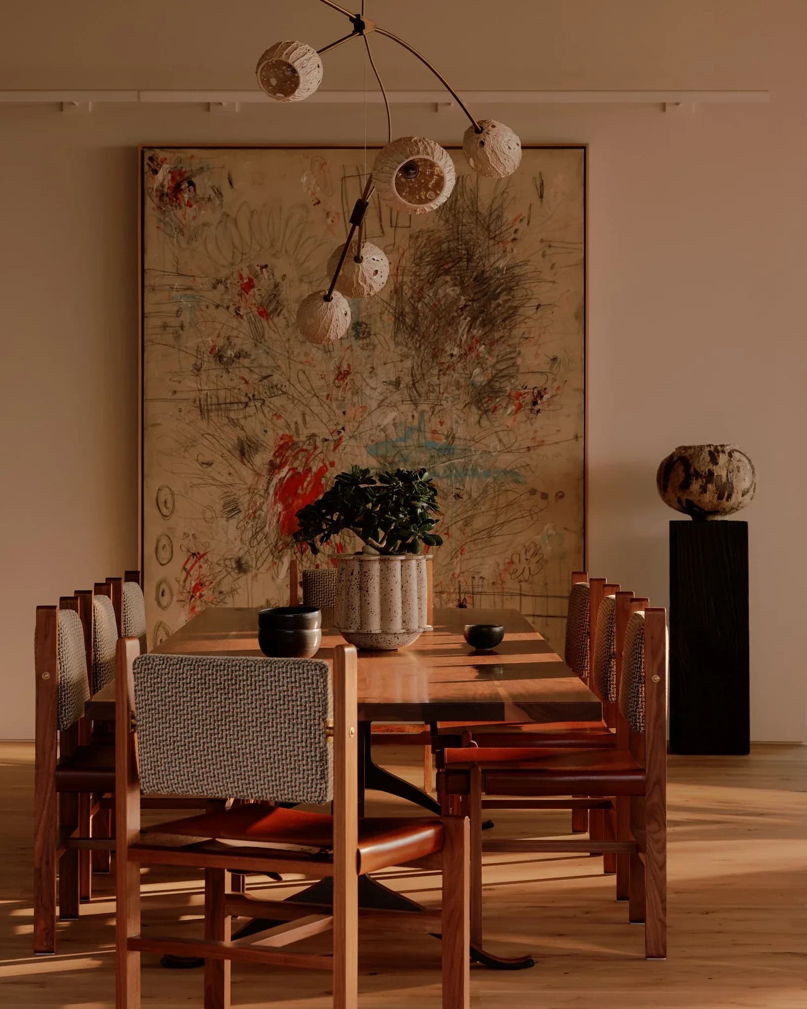 Minimalist dining room with warm wood chairs, striped upholstery, botanical wall art, hanging mobile, and ceramic vessels by Claudia Janell.