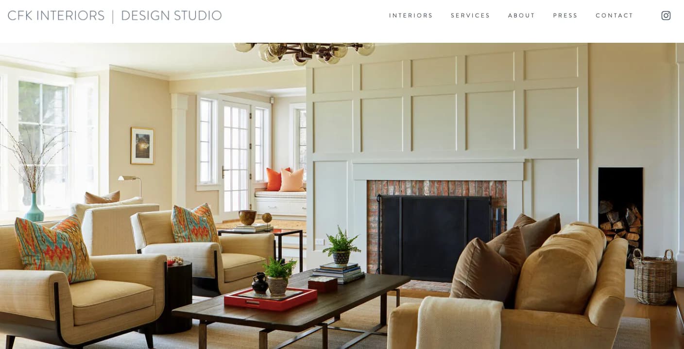 Elegant living room with cream-colored upholstered seating, paneled fireplace wall, dark coffee table, and warm neutral palette by Claudia Kalur.
