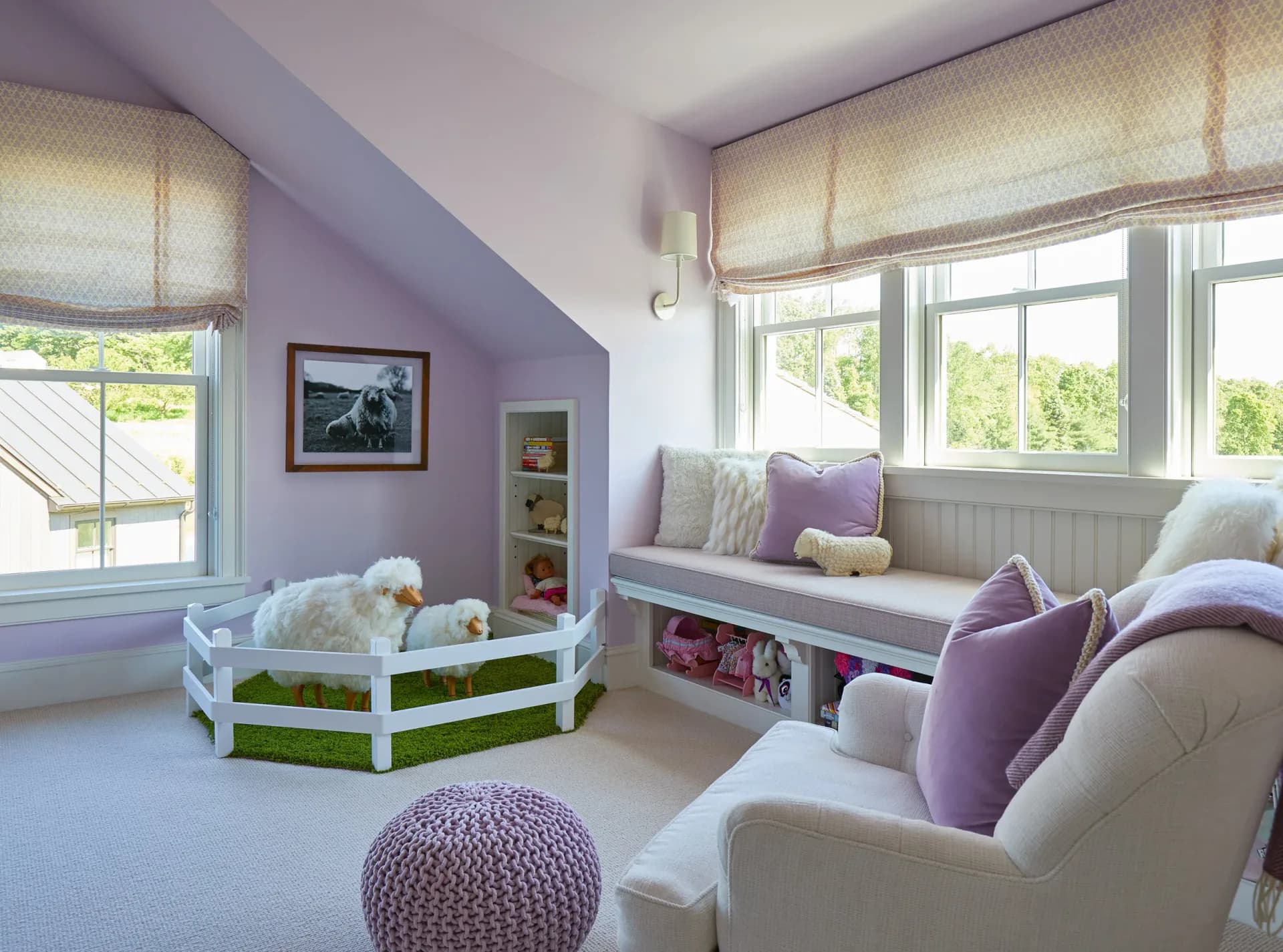 Purple and white children's playroom with built-in window seating, green storage baskets, and soft furnishings by Claudia Kalur.