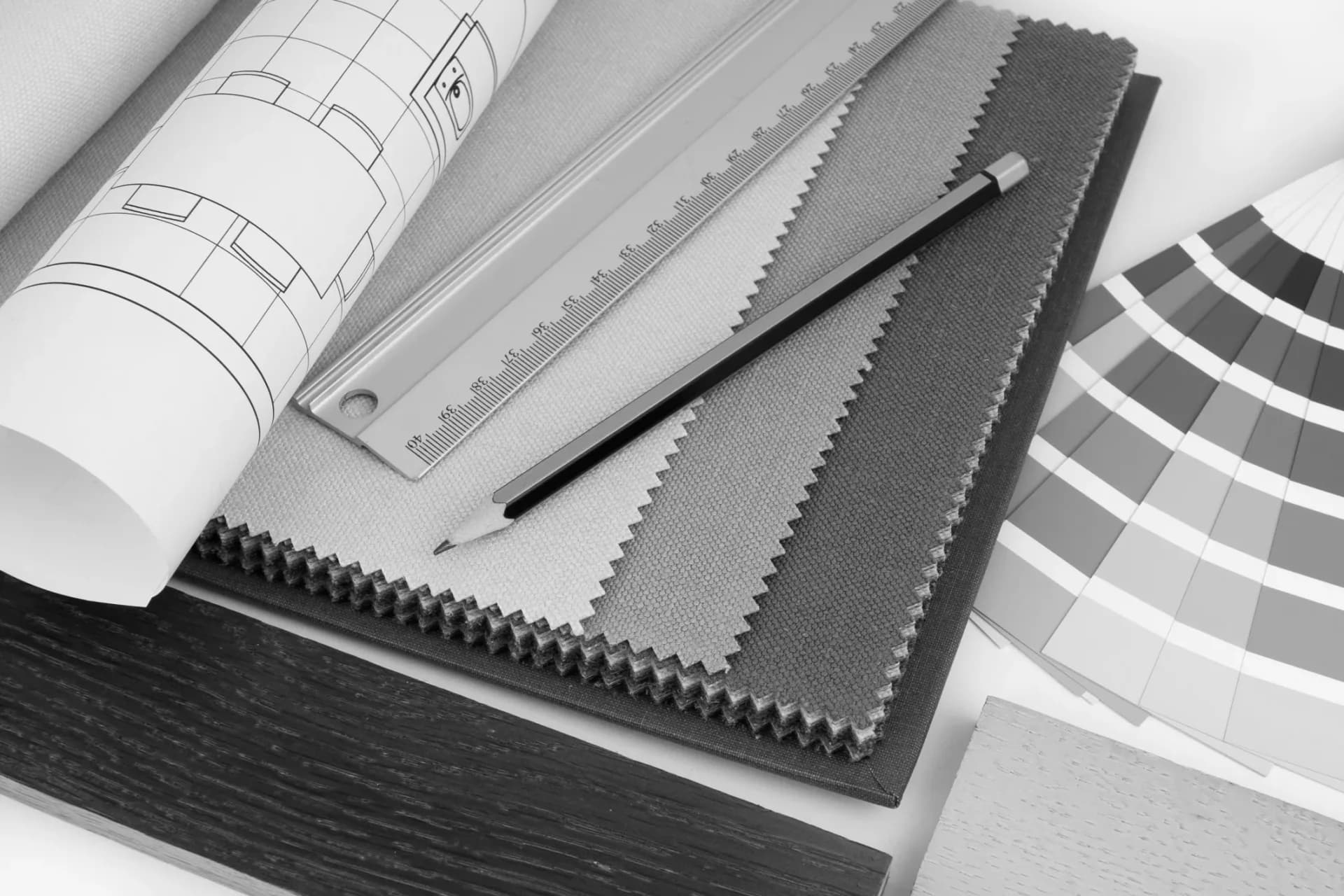 Material samples and design tools including fabric swatches, architectural blueprints, color palette guide, and ruler arranged on a work surface by Clemence Bouchabake.