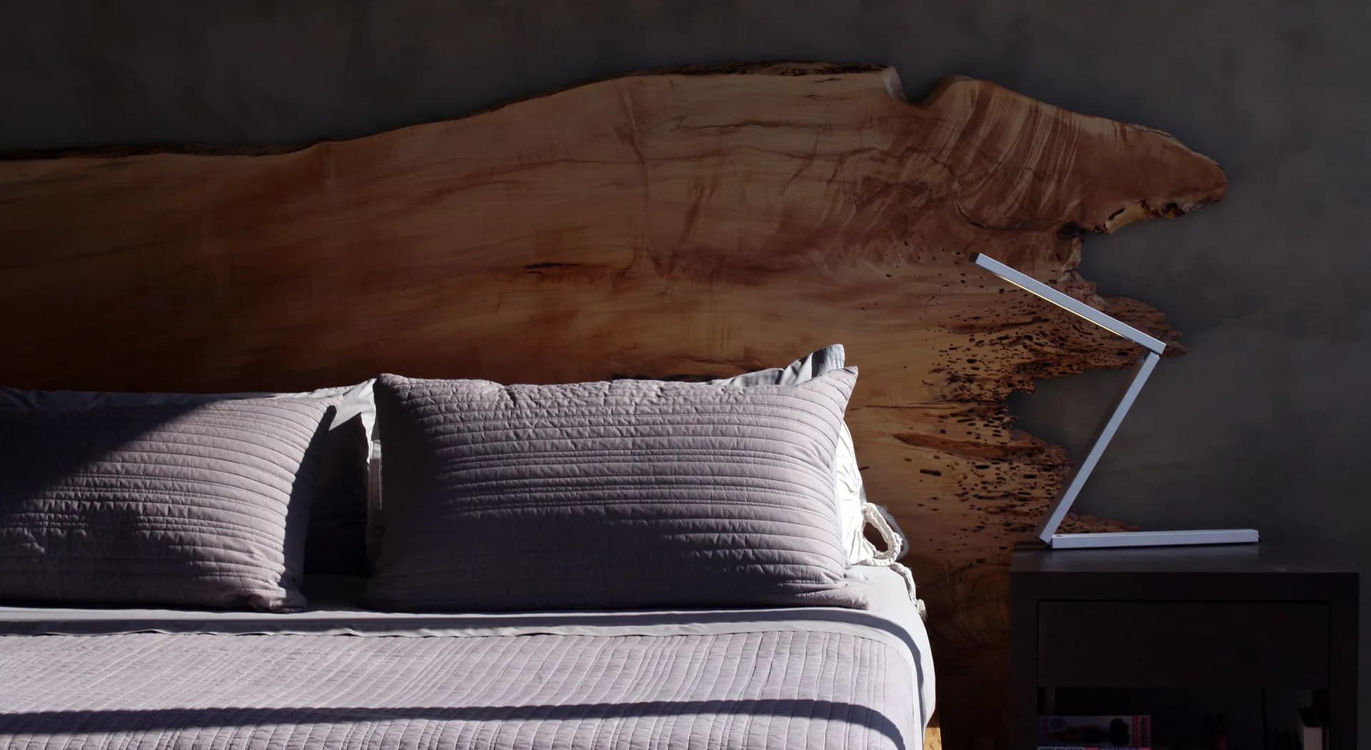Minimalist bedroom with warm wood headboard, crisp white bedding, layered pillows, and geometric wall art by Clodagh.