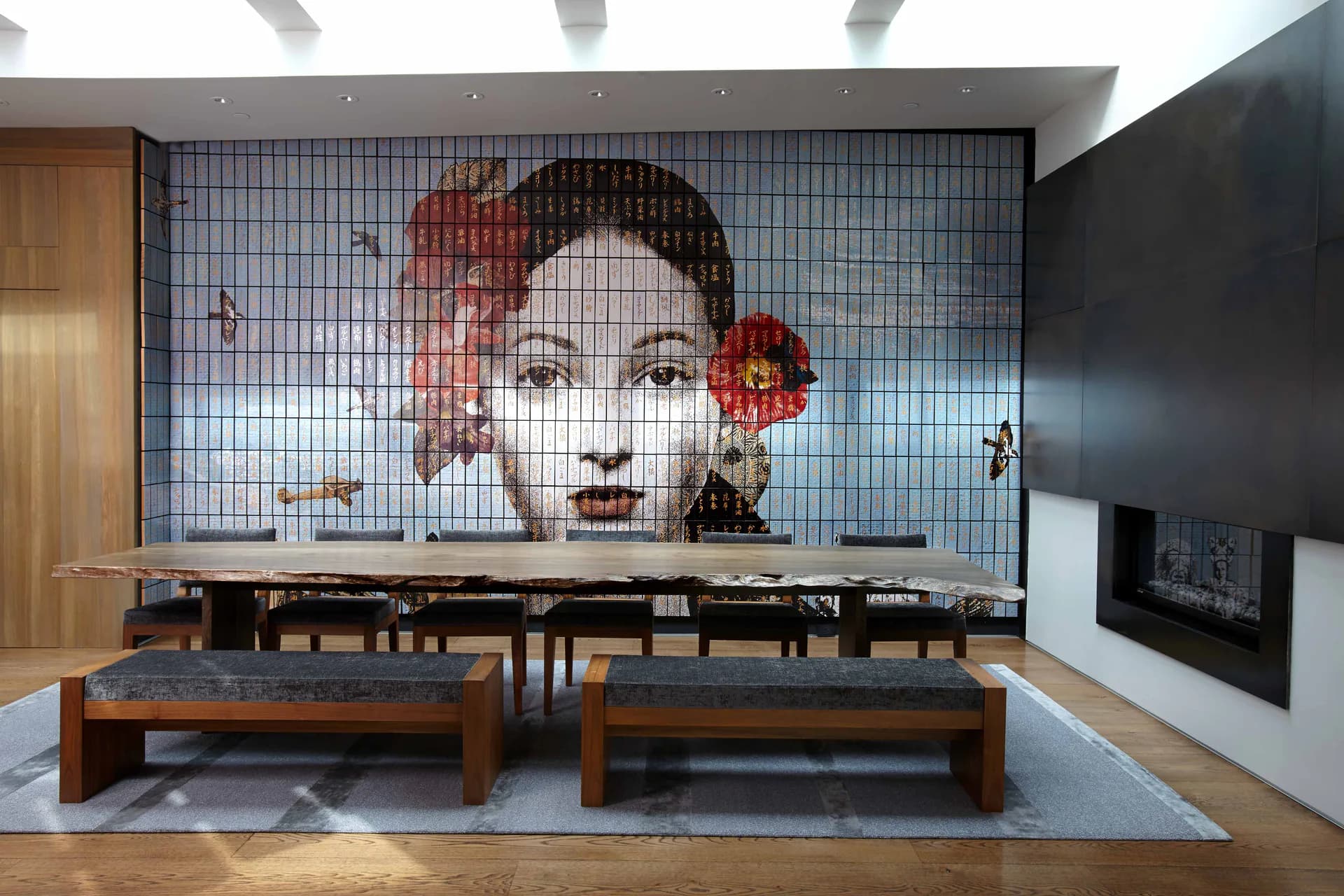 Recreation room features two wooden pool tables beneath a striking mosaic portrait wall installation, modern lighting, and dark accents by Clodagh.