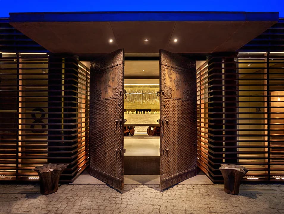Grand entrance with massive bronze curved doors, brick walls, warm ambient lighting, and minimalist furnishings by Clodagh.