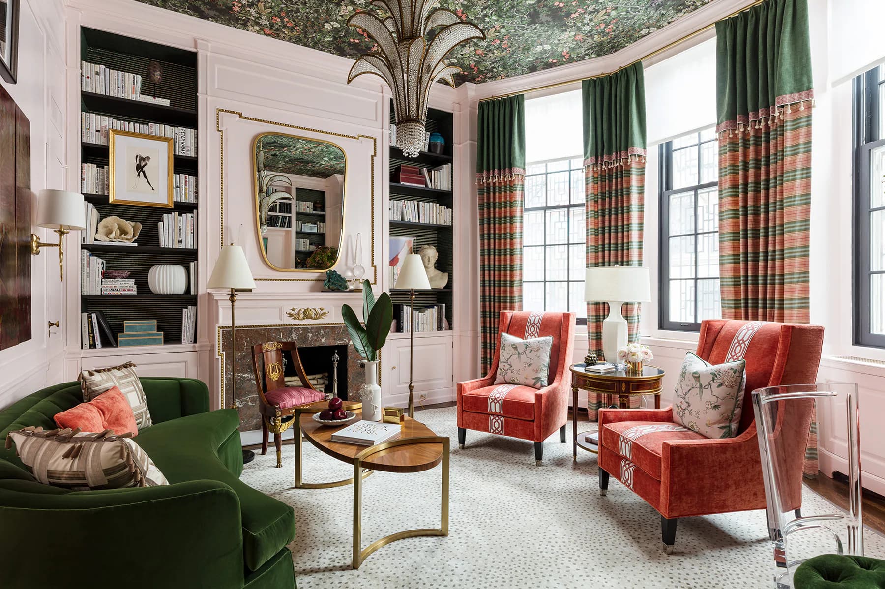 Sophisticated living room with pink walls, green velvet seating, coral patterned chairs, brass accents, and botanical wallpaper ceiling by Corey Damen Jenkins.
