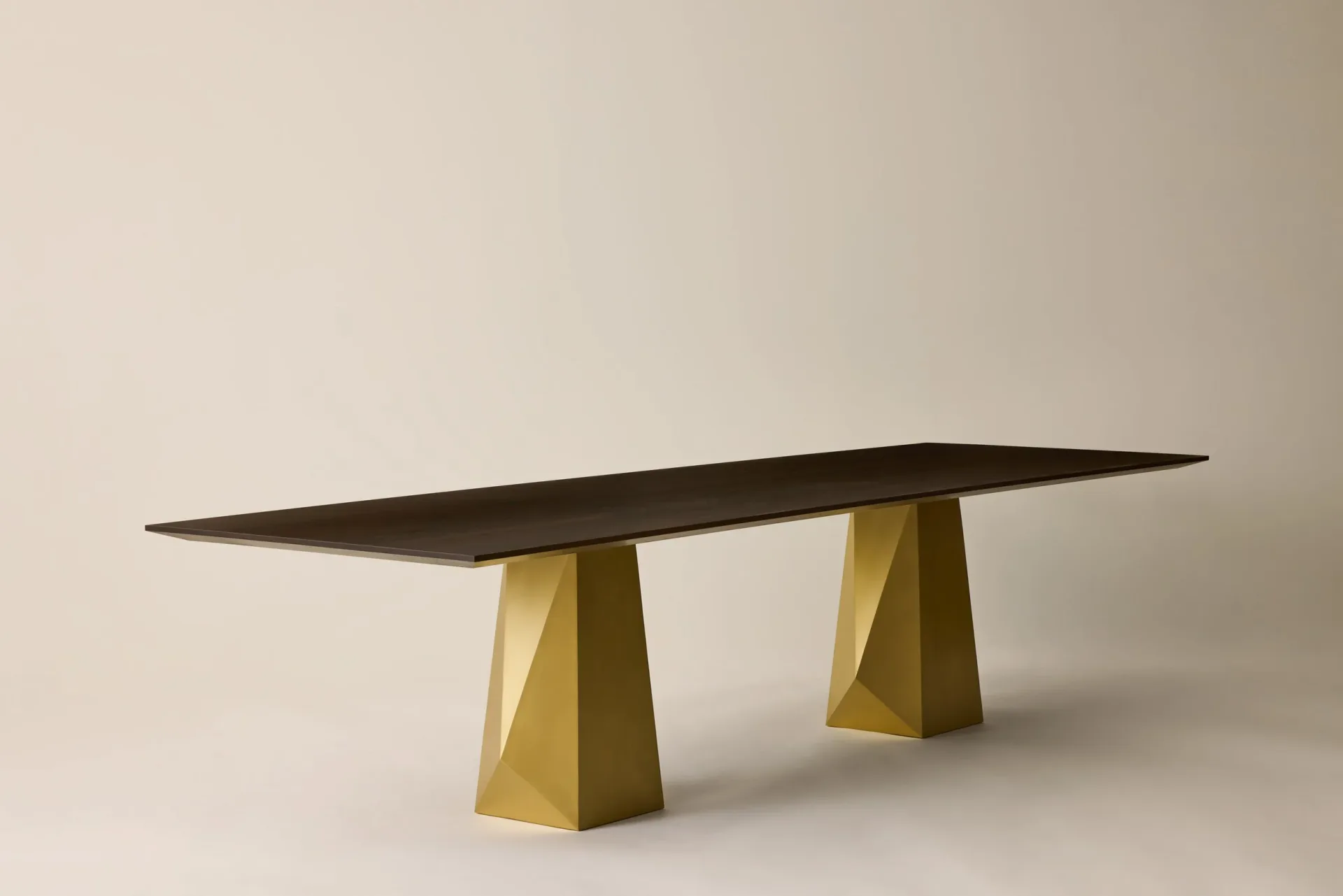 Modern dining table with dark top and geometric golden trapezoid legs on neutral background by Crystal Ellis.