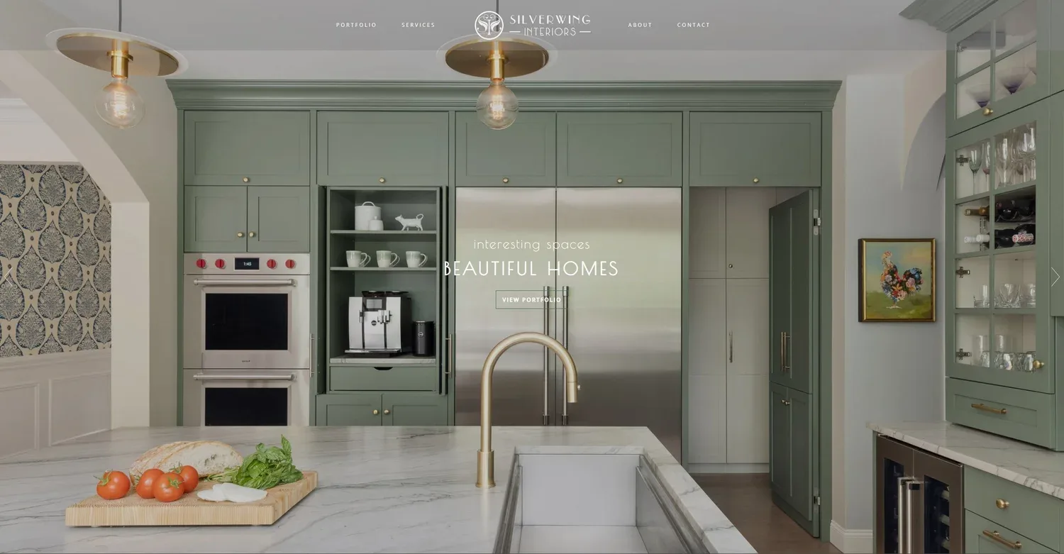 Modern kitchen with sage green cabinetry, stainless steel appliances, white marble countertops, and brass pendant lighting by Crystal Maki.