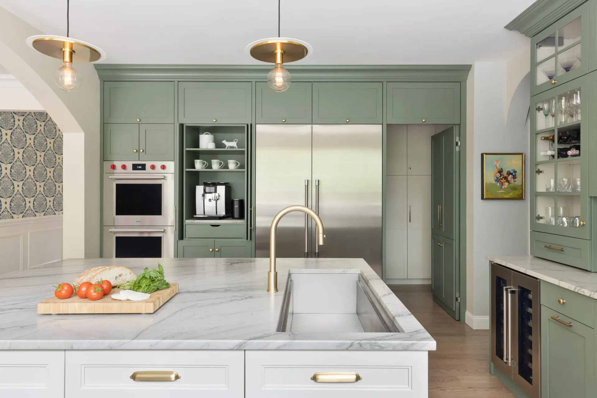Modern kitchen with sage green cabinetry, white marble island, stainless steel appliances, and brass pendant lighting by Crystal Maki.