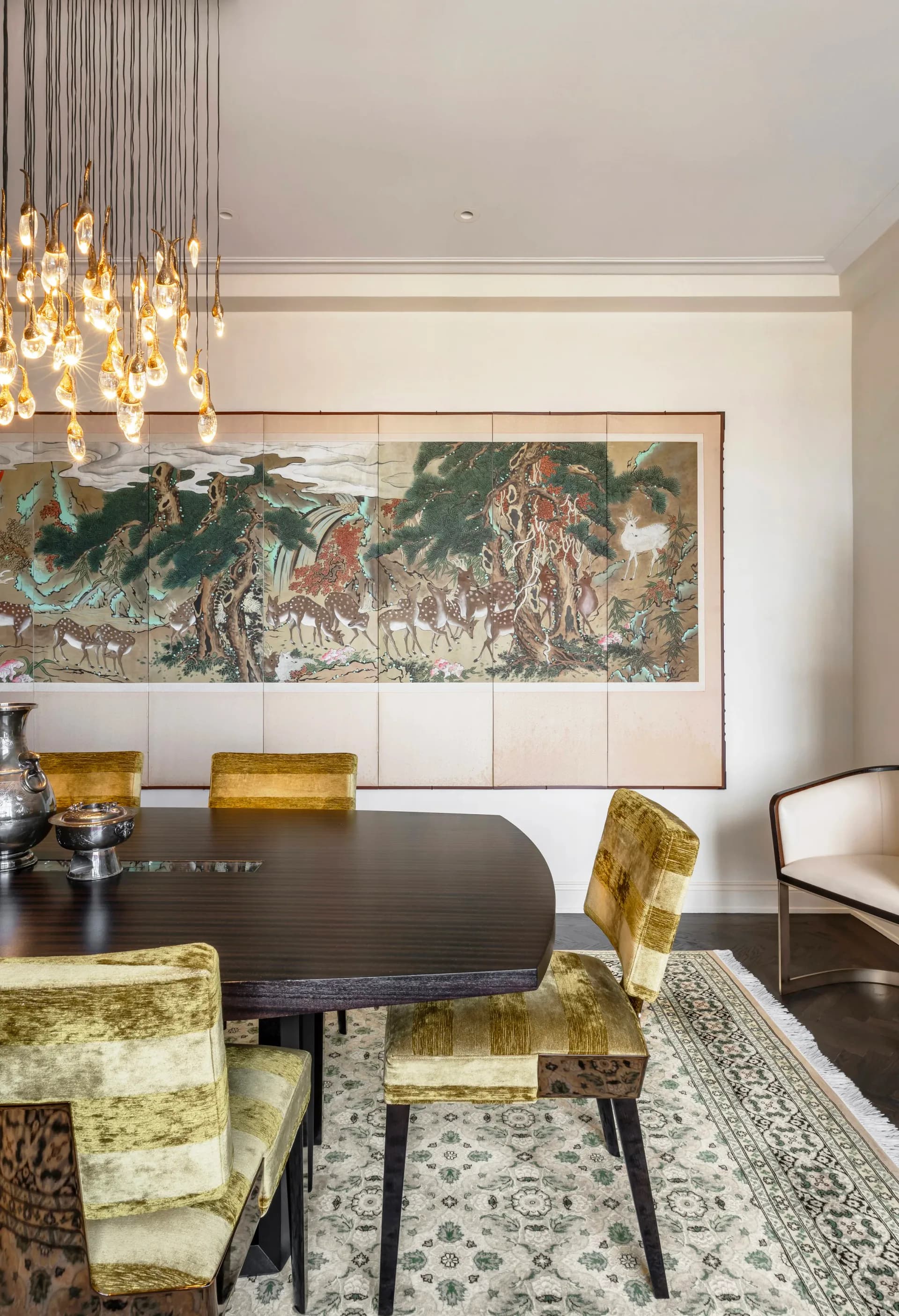Modern dining room with black oval table, chartreuse velvet chairs, pendant lighting, and large framed landscape artwork above white paneling by Cynthia Peralta-Brito.