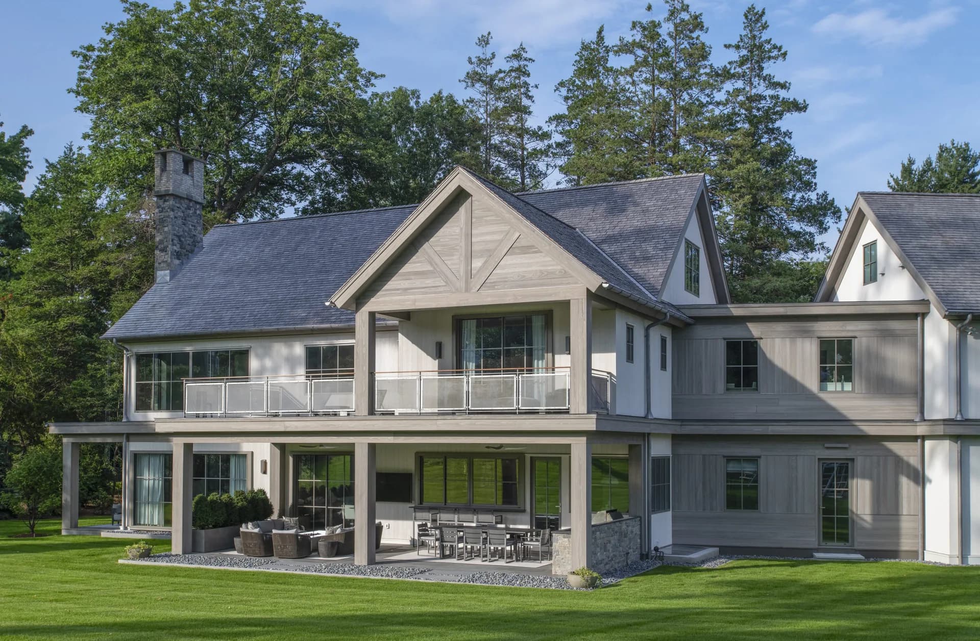 Modern farmhouse exterior with white and gray façade, gabled roofline, covered porch, manicured lawn, and mature trees, designed by Cynthia Vengrow.