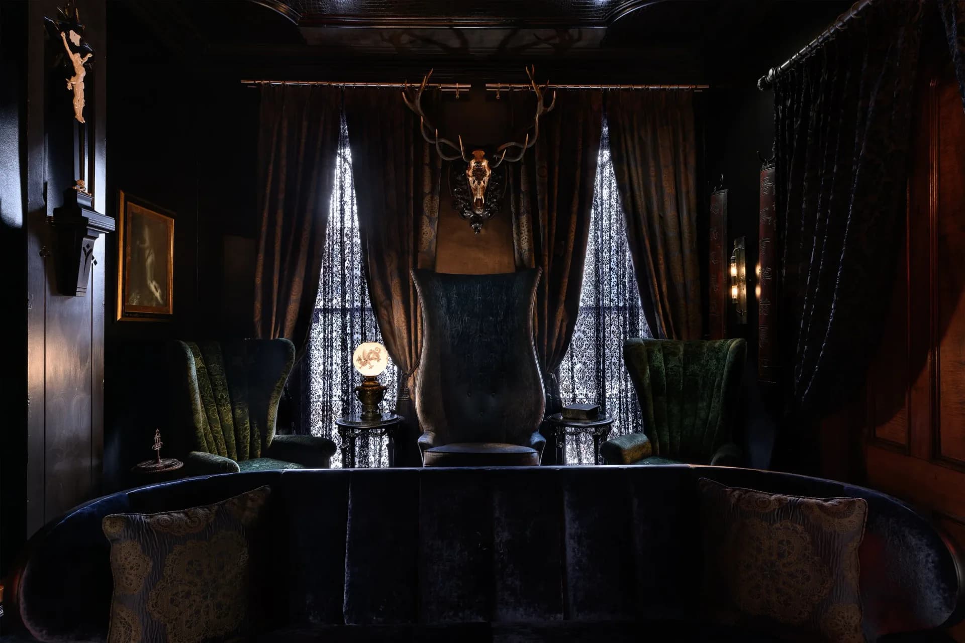 Luxurious dark bar interior with black velvet seating, golden antler sculpture, crystal pendant lighting, and jewel-toned curtains by Dakota Nesselbush.