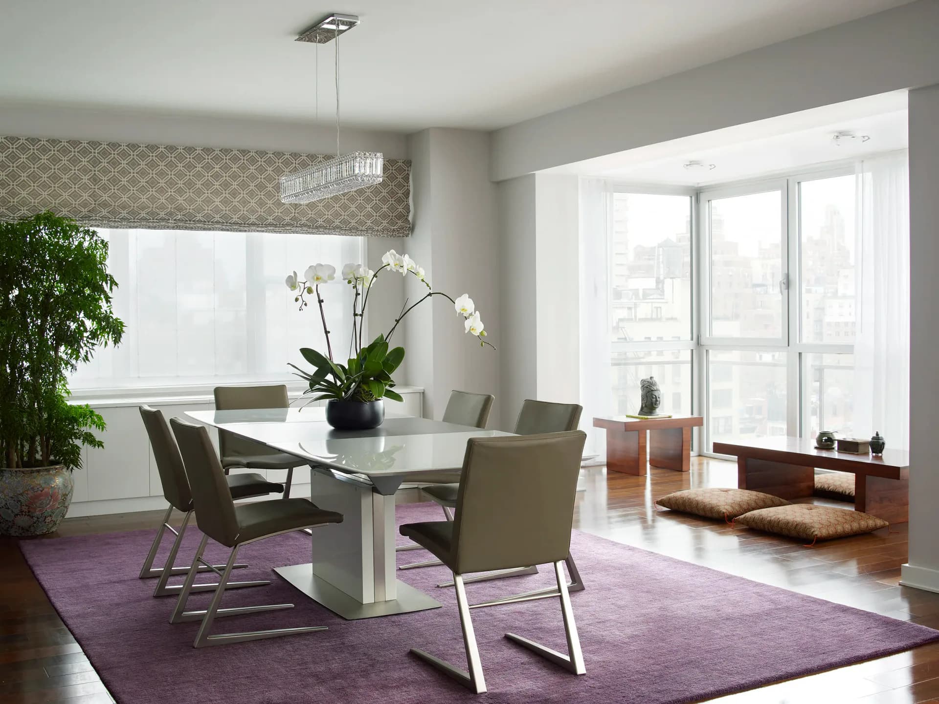 Modern dining room with white pedestal table, gray chairs, and purple area rug, featuring floor-to-ceiling windows and minimalist furnishings by Damiano Geraci.