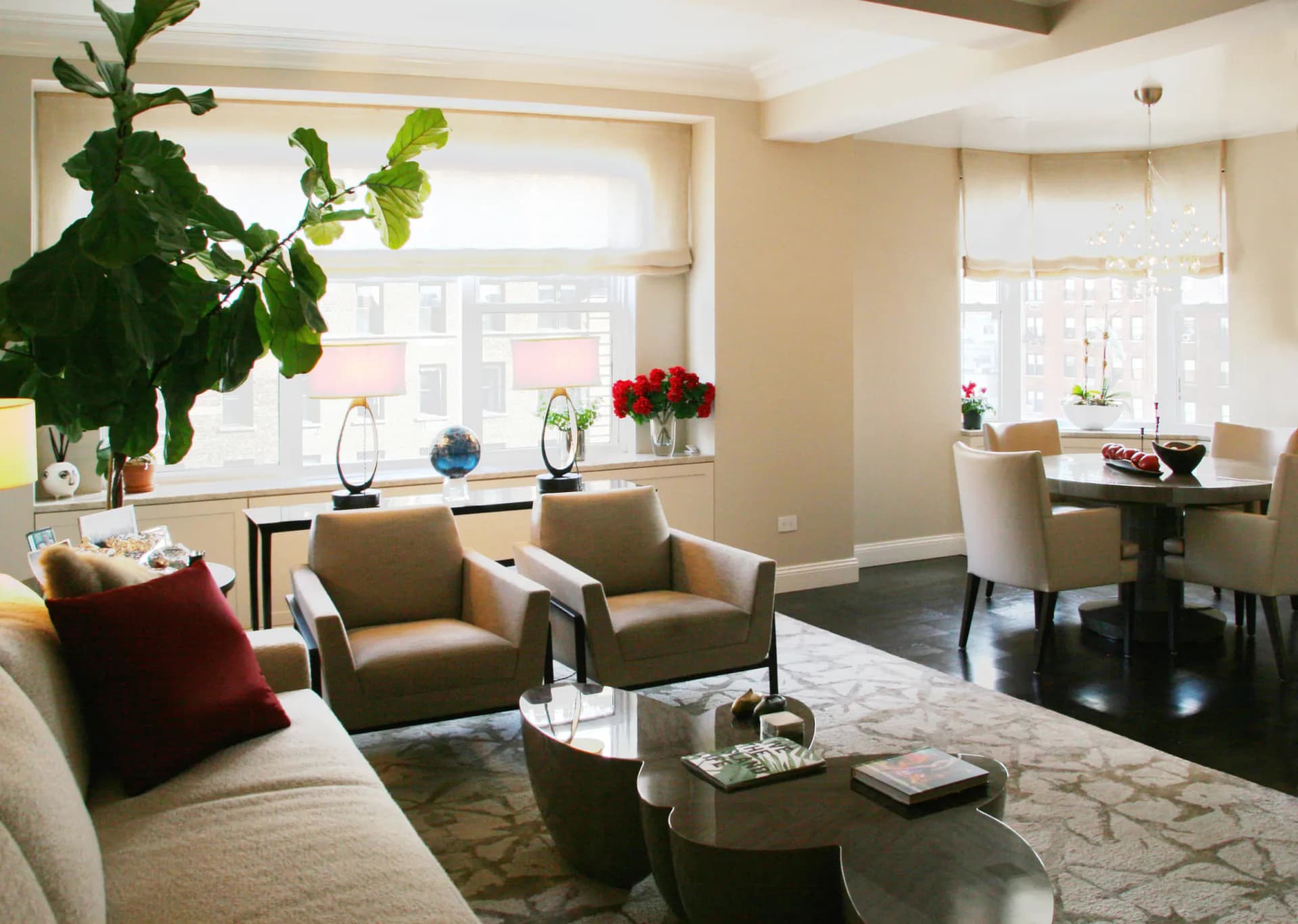 Warm contemporary living room with taupe upholstered seating, black accent table, and large windows overlooking cityscape, designed by Damiano Geraci.