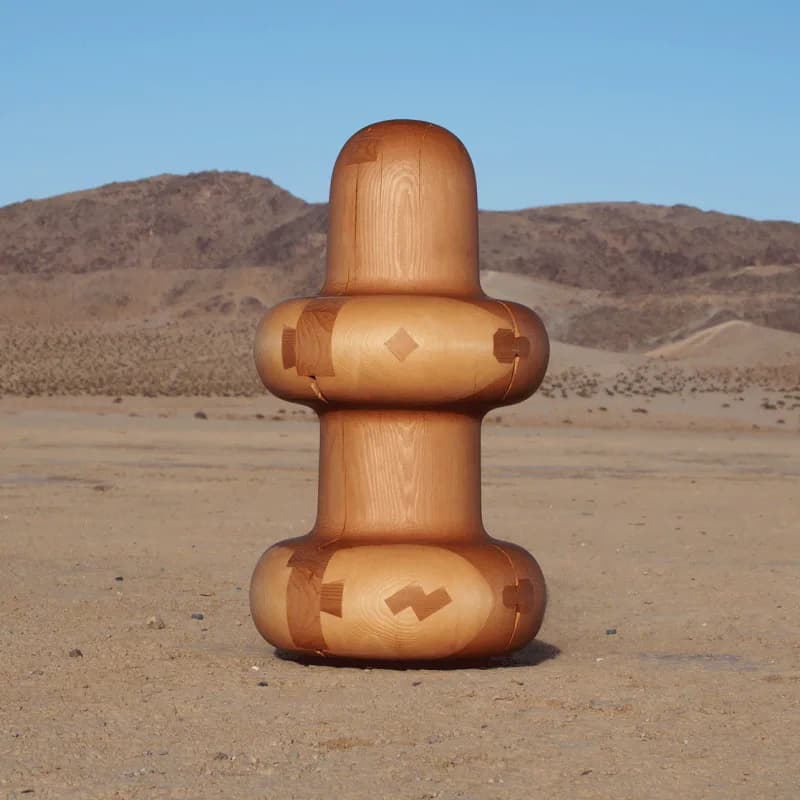 Wooden sculptural installation in desert landscape featuring stacked geometric forms with carved diamond and rectangular motifs by Dan John Anderson.