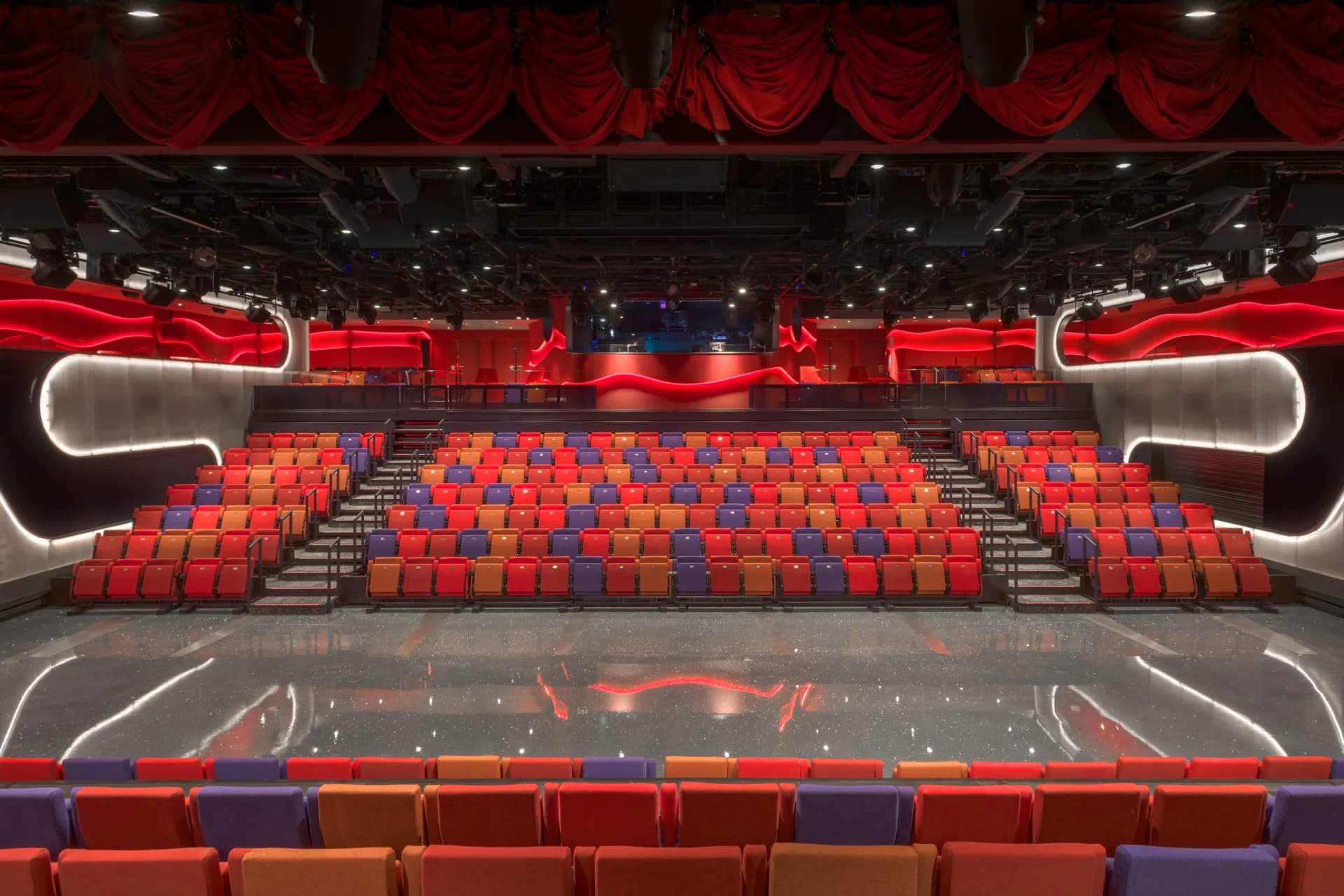 Modern cinema auditorium with tiered red seating, dramatic red neon architectural elements, and dark ceiling with recessed lighting by Dan Wood.