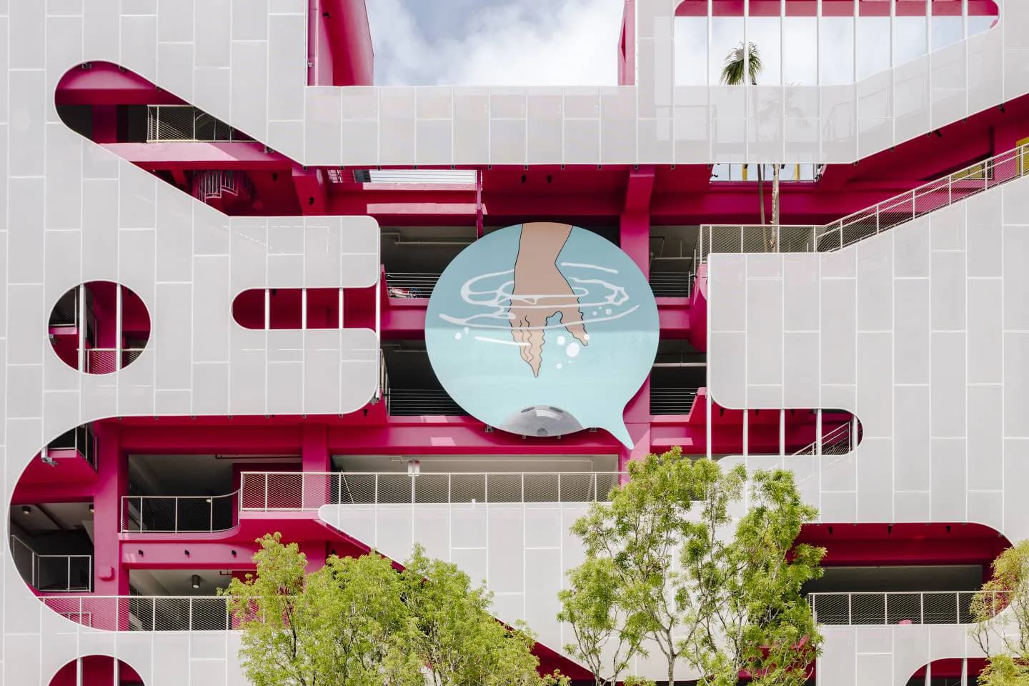 Aerial view of a modernist building with bold burgundy curved architectural elements and white gridded facade, featuring a central circular skylight, designed by Dan Wood.