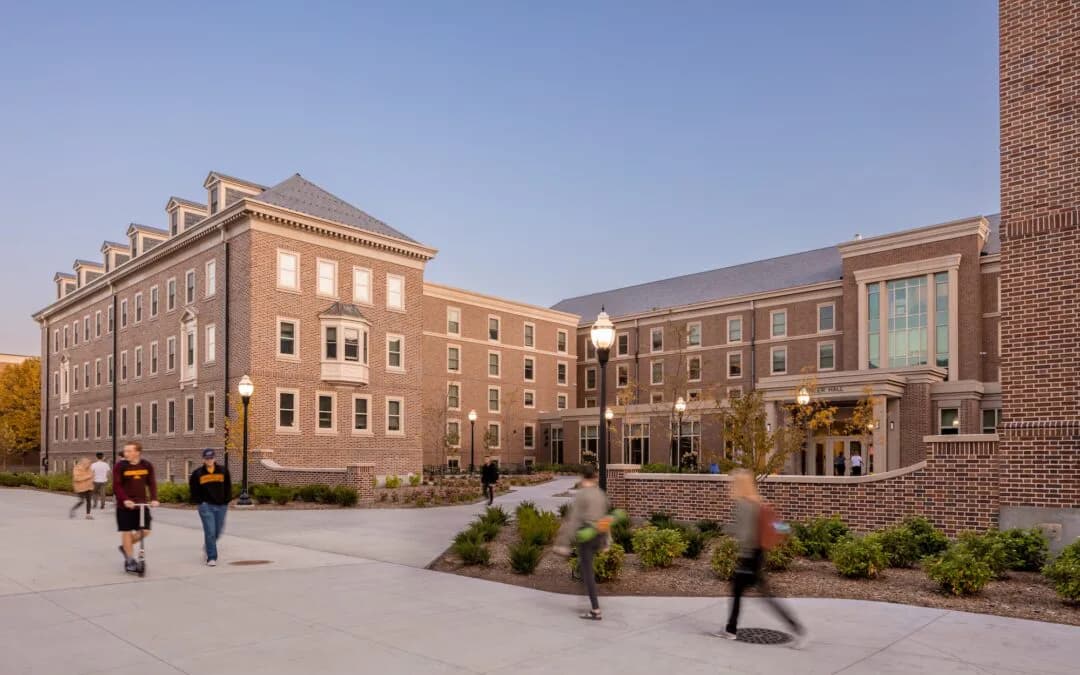 Brick and stone academic campus courtyard with modern institutional buildings, landscaped plantings, and plaza gathering space by Dana McCarty.