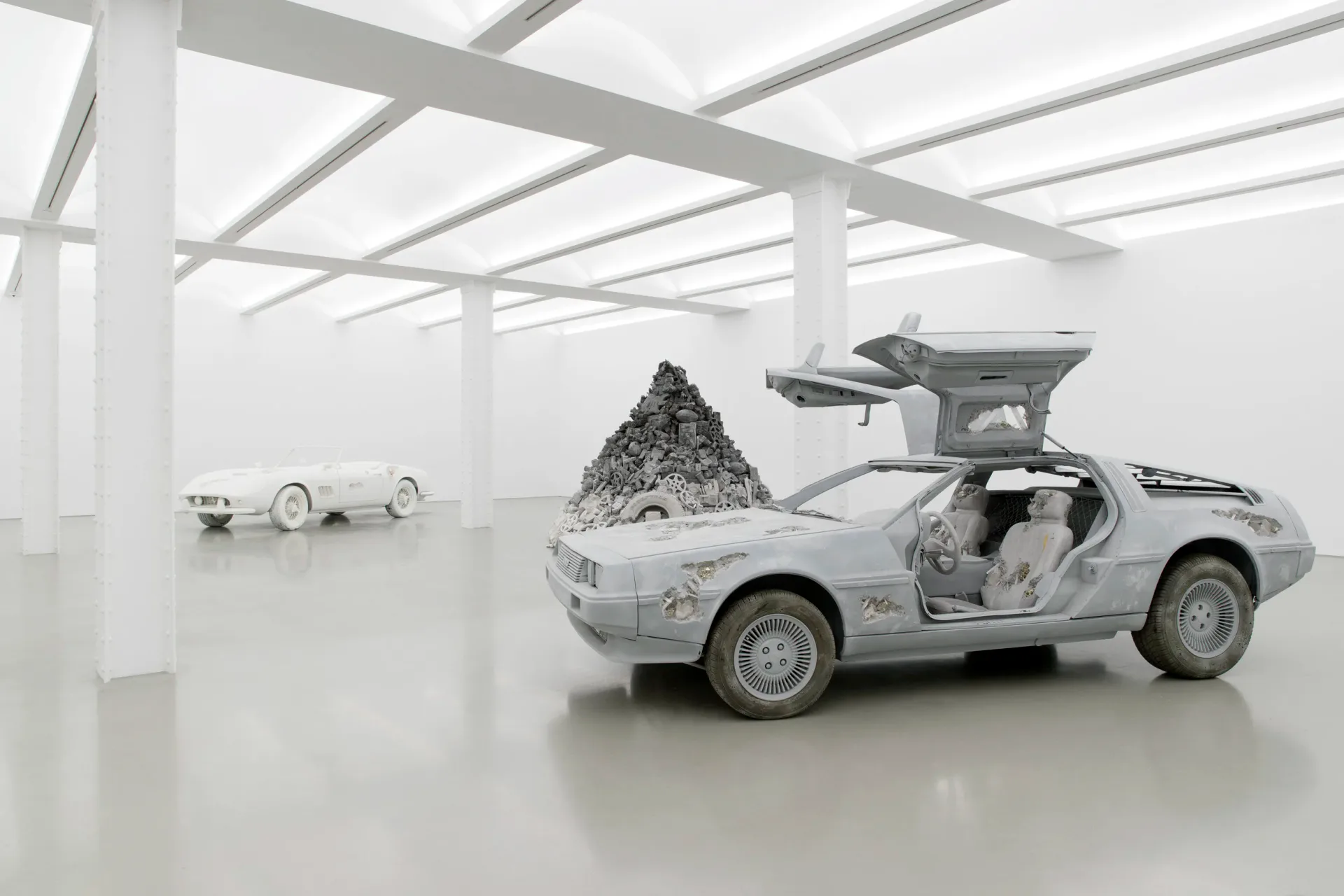 Minimalist white gallery space with geometric sculptures and a futuristic car with gull-wing doors, rendered installation by Daniel Arsham.