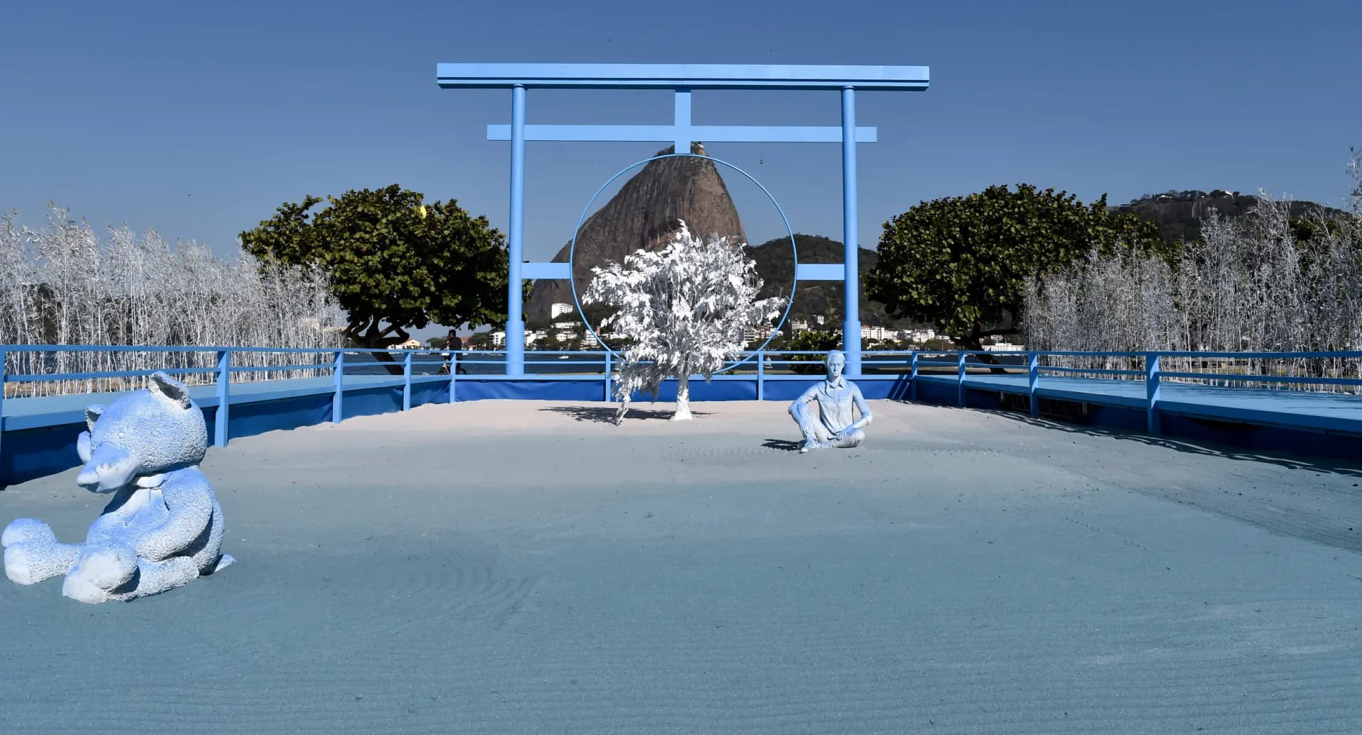 Minimalist blue and white architectural installation with geometric forms, sculptural elements, and framed mountain vista by Daniel Arsham.