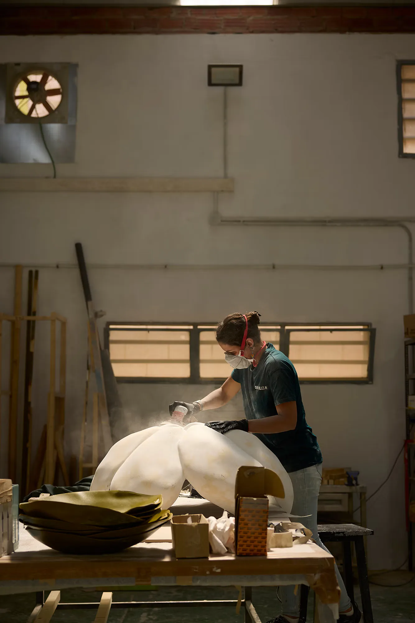 Craftsperson working on a white sculptural form in a bright studio workshop with wood paneling and industrial lighting by Daniel Maldonado.