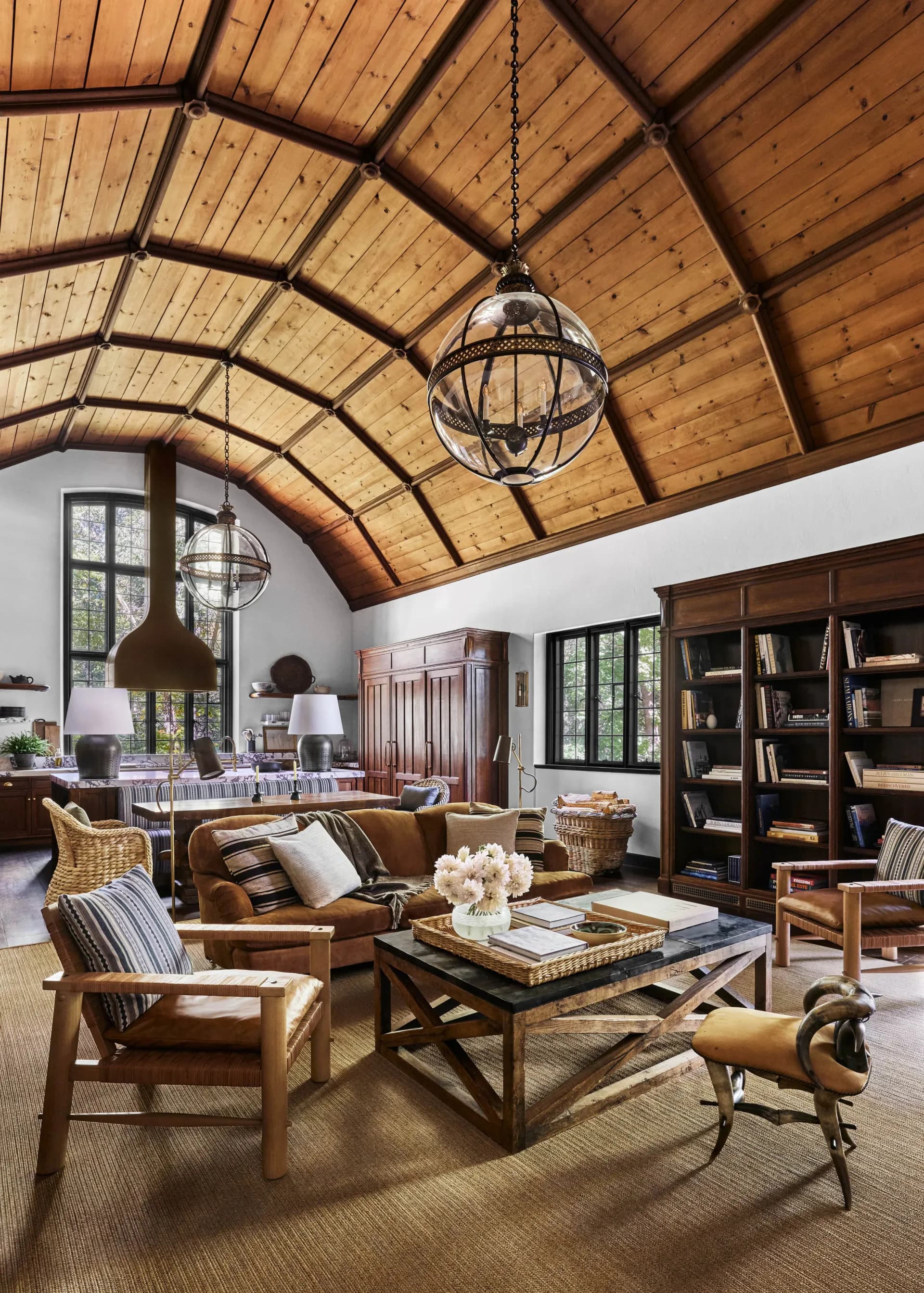 Modern living room with arched wood ceiling, leather armchairs, built-in bookshelves, and globe pendant lighting by Danielle Peterfy.