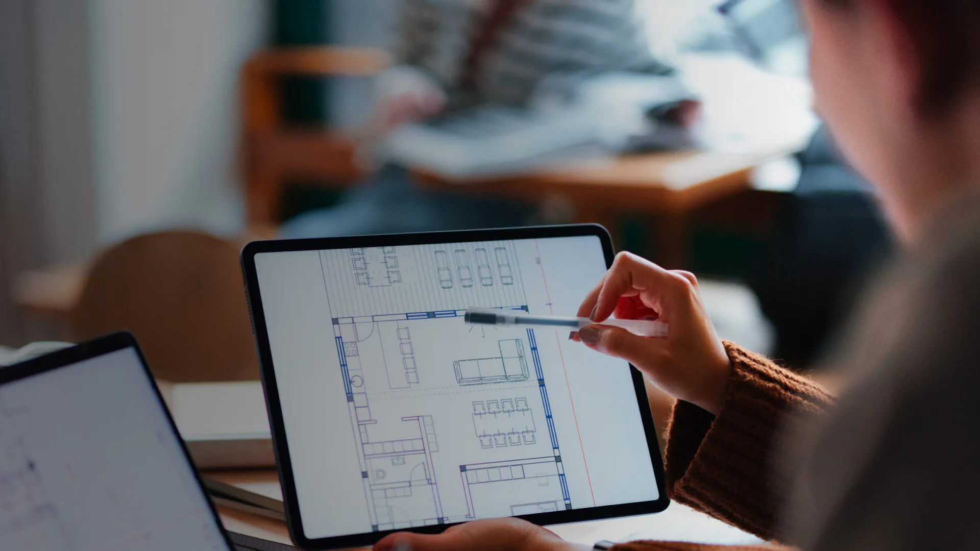 Designer reviews architectural floor plans and layouts on tablet during collaborative workspace session by Danielle Rapanaro.