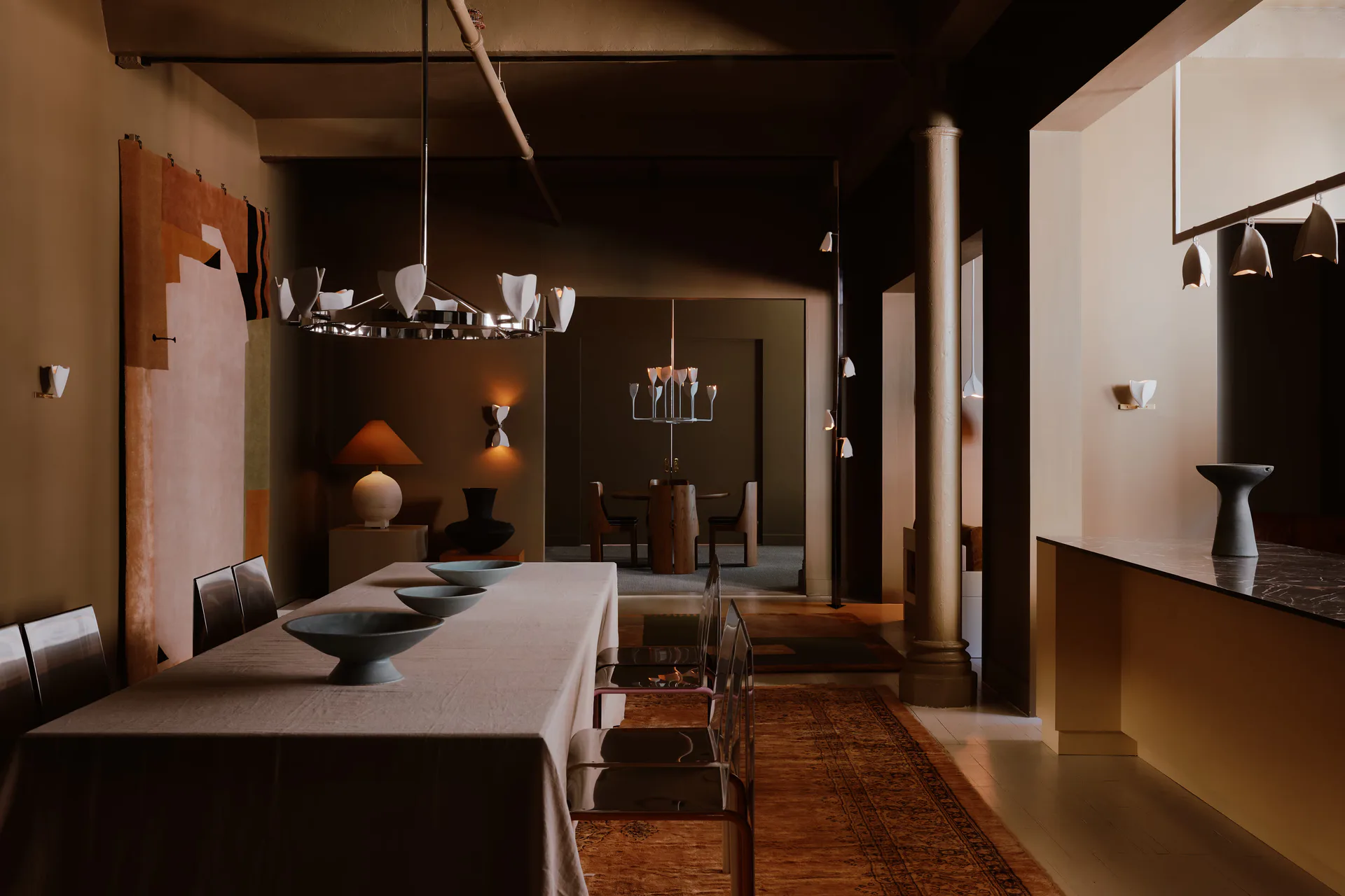 Contemporary interior showroom with warm terracotta and dark tones, featuring display niches, dining table, and sculptural lighting by Danny Kaplan.