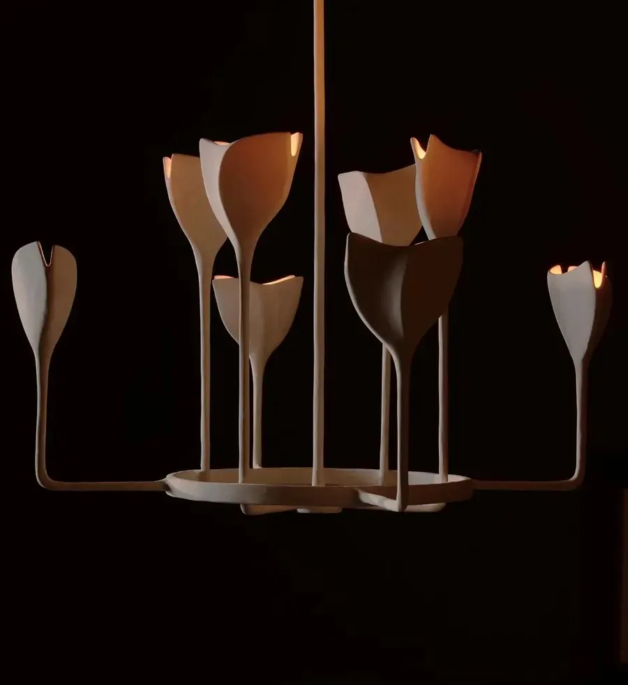 Sculptural brass chandelier with organic petal-like forms and cream silk accents, arranged in ascending heights against black background by Danny Kaplan.