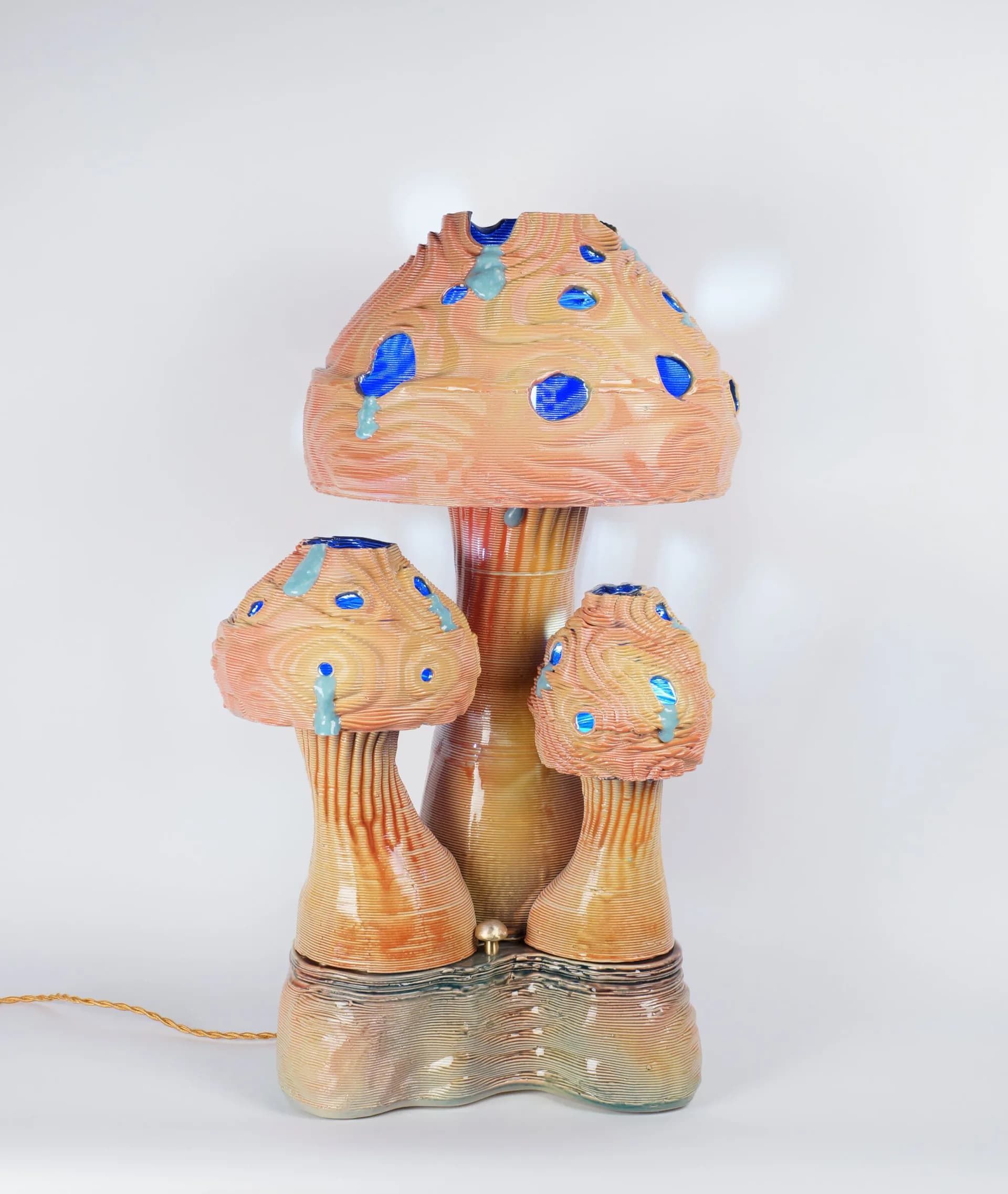 Wooden mushroom-shaped sculptural lamp with peach-toned finish and blue decorative accents, featuring three tiered caps and a cylindrical stem with glass base by Dara Schaefer.