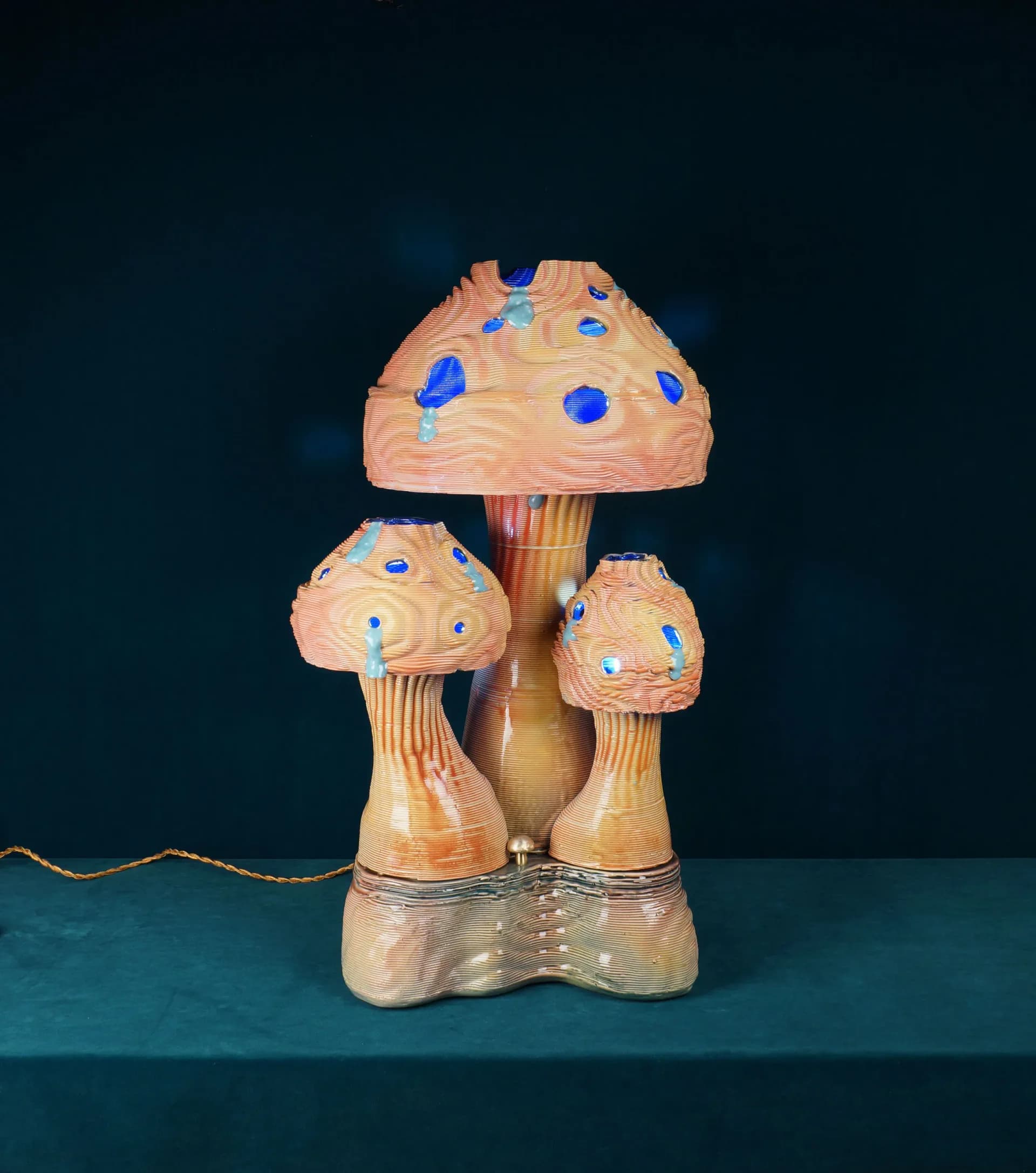 Wooden mushroom-shaped sculptural installation with peach-toned caps adorned with blue and cyan accents, displayed on a teal surface by Dara Schaefer.