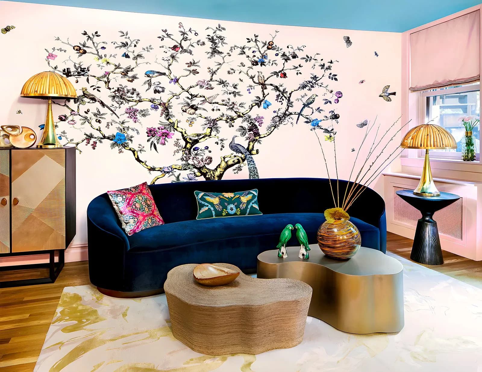 Modern living room with curved navy sofa, tree mural wallpaper, brass dome lamps, and geometric wood coffee tables by Daria Demin.