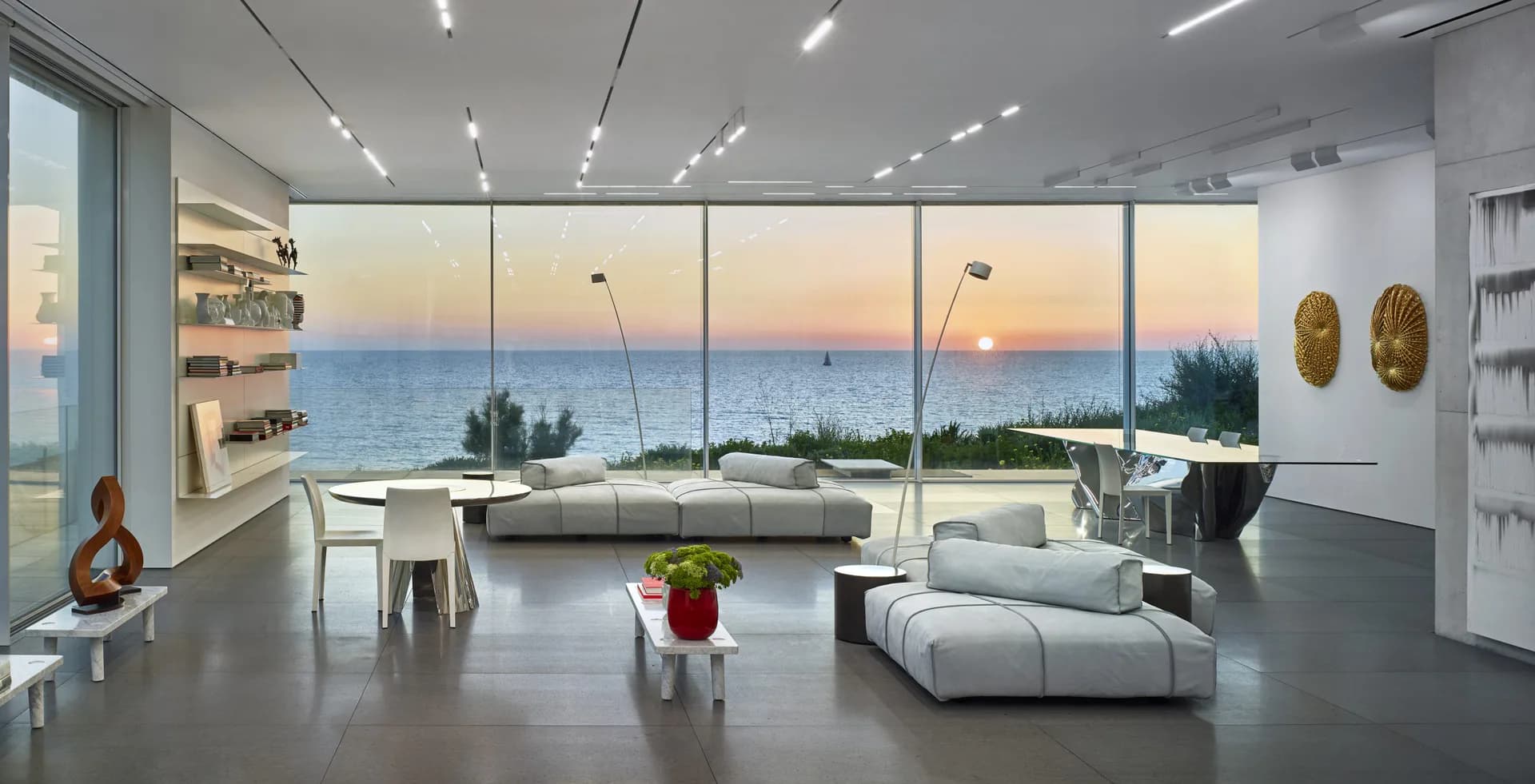 Modern luxury penthouse with floor-to-ceiling windows overlooking sunset seascape, minimalist white furnishings, and polished concrete floors by Daria Karelina.