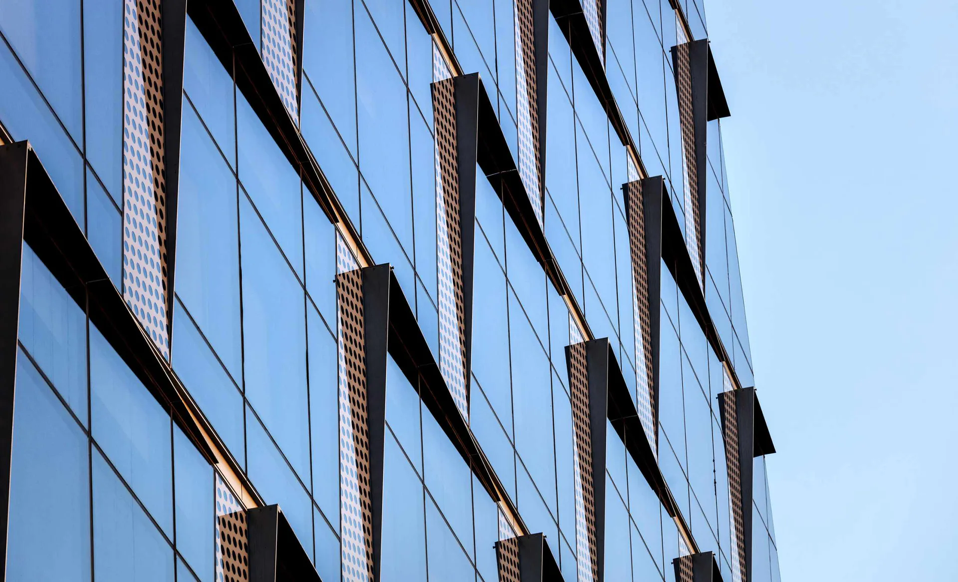 Modern glass and metal facade featuring reflective blue-tinted windows with bronze/copper mullions and geometric horizontal banding by David Aboyoun.