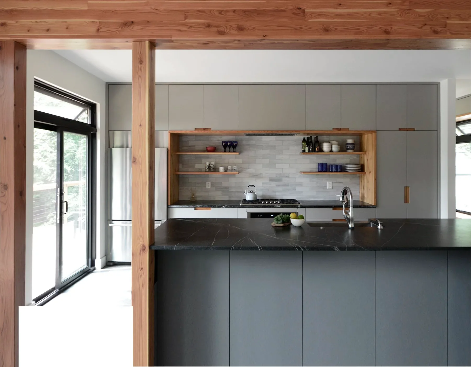 Modern kitchen with dark lower cabinetry, light upper cabinets, wooden shelving, black countertop, and exposed wood beams by David E Fredlund.