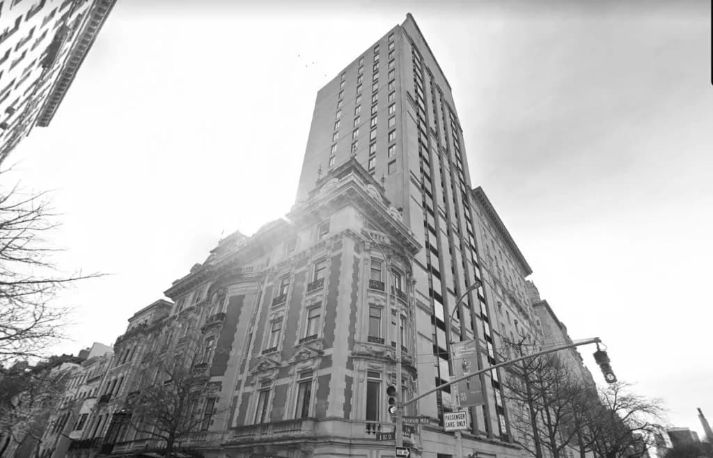 Exterior view of a tall residential tower with classical ornamental base and modern upper stories against an overcast sky by David Jhee.