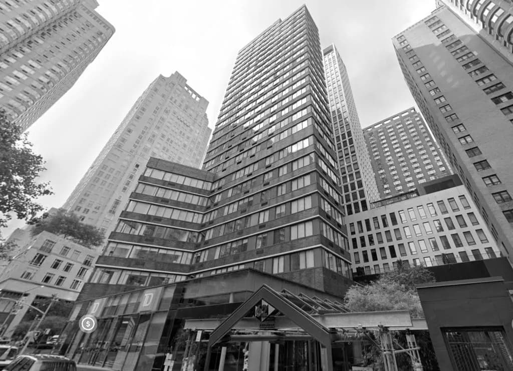 Upward-looking urban street view featuring towering modernist high-rises surrounding a small historic building, photographed in black and white by David Jhee.