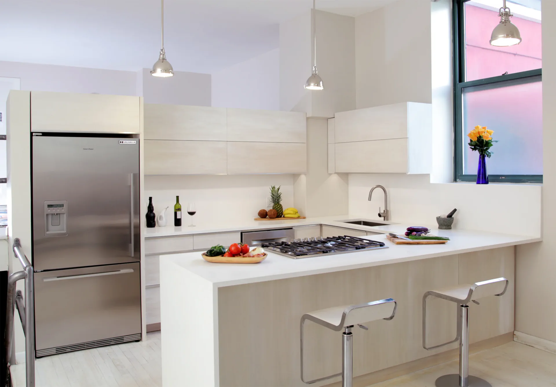 Modern kitchen with white cabinetry, waterfall island countertop, stainless steel appliances, and pendant lighting designed by David Jones.