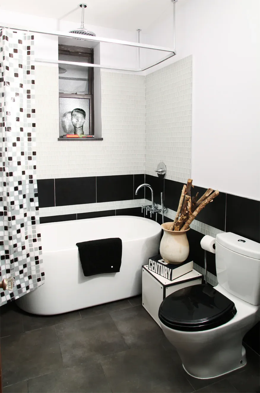 Modern bathroom with black and white tile work, curved white soaking tub, black toilet, and geometric patterned shower curtain by David Jones.