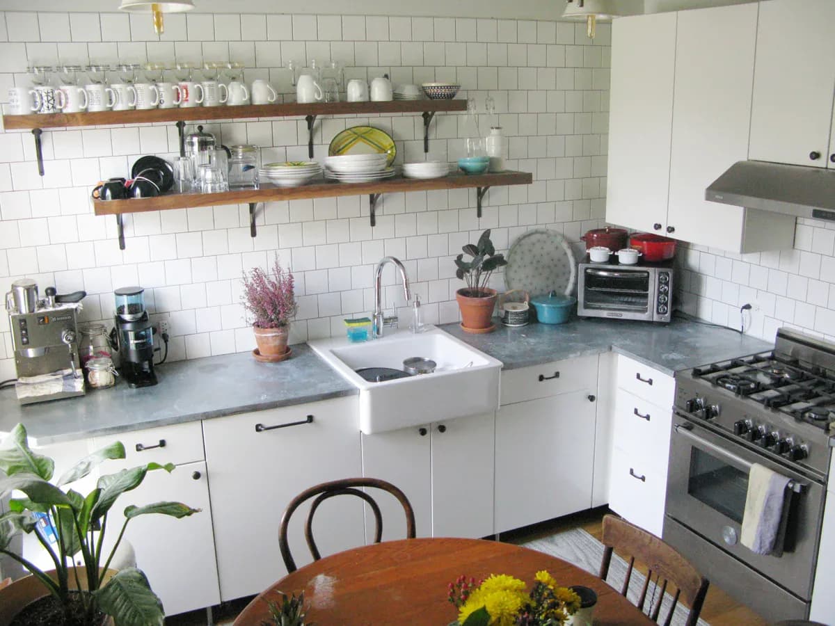 Modern kitchen with white cabinetry, subway tile backsplash, open wooden shelving, stainless steel appliances, and blue-gray countertops by David Jones.