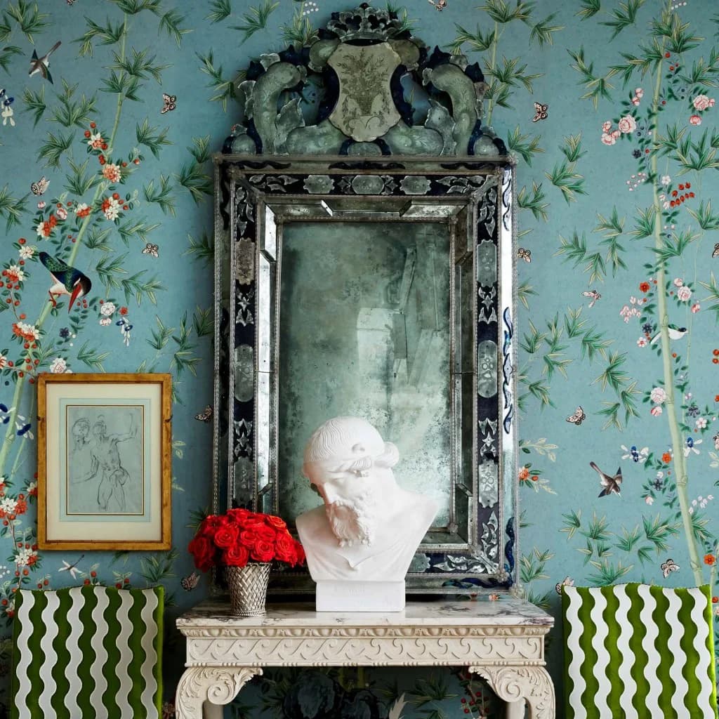 Turquoise wallpapered interior with ornate black mirror, white bust sculpture, red flowers, and decorative mantelpiece by David Kaihoi.