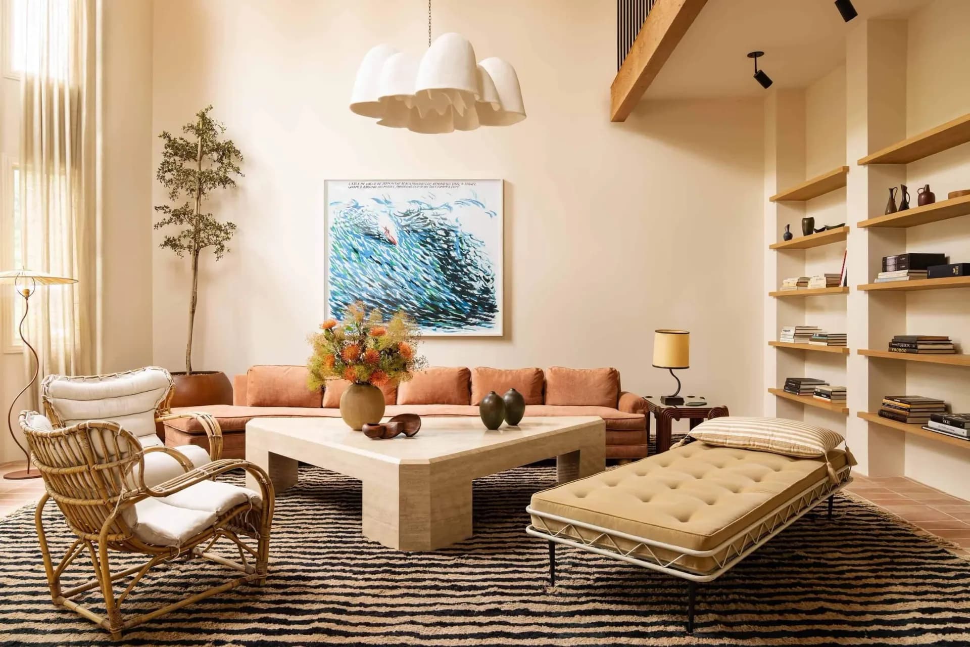Sophisticated living room with coral sofa, cream travertine coffee table, woven pendant light, and ocean artwork by David Lucido.