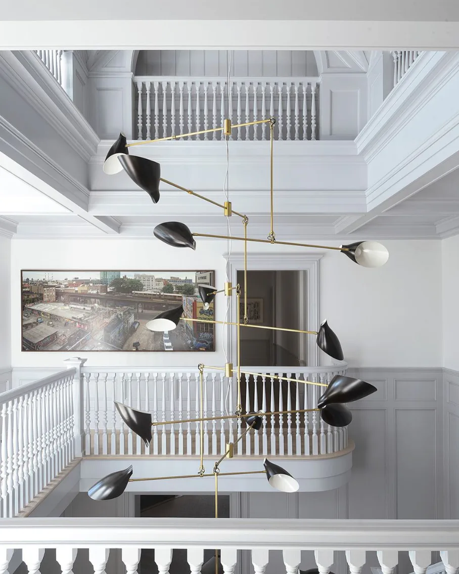 Multi-story atrium with brass articulated pendant lights suspended across white walls and railings by David Weeks.