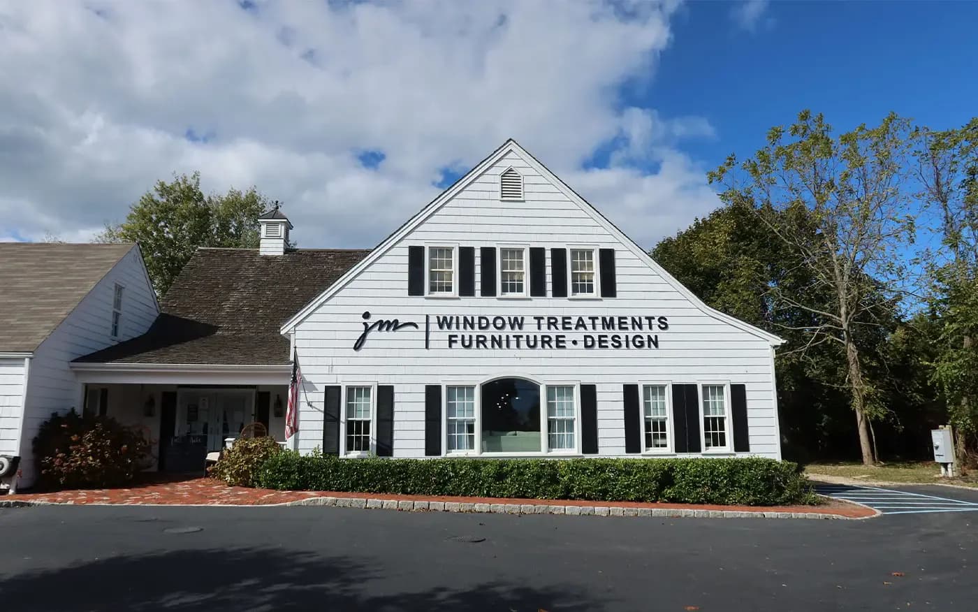 White colonial storefront with black shutters and signage for window treatments, furniture, and design services by Deanna Colondona.